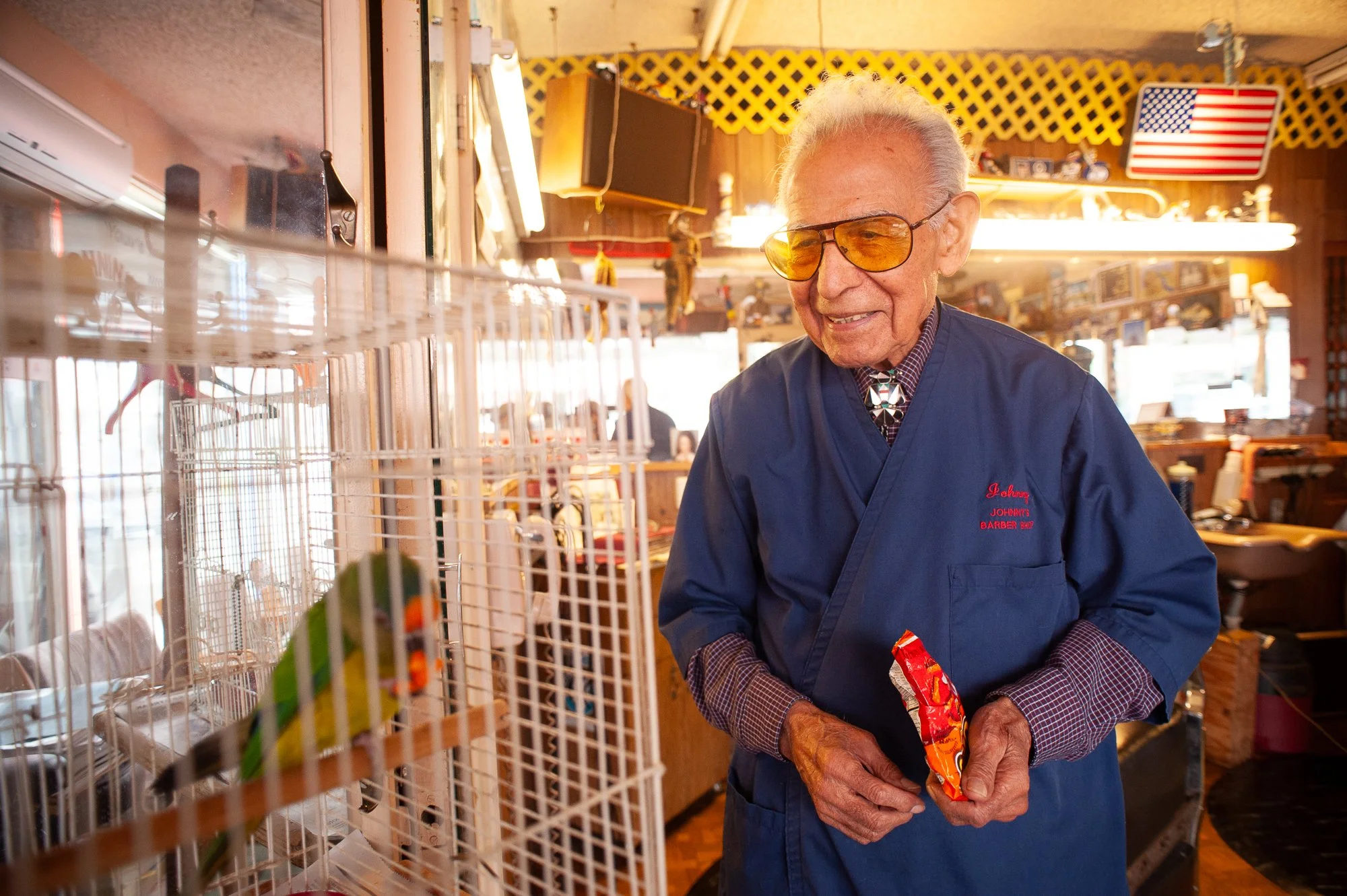 An old school barber smiles while watching his pet bird
