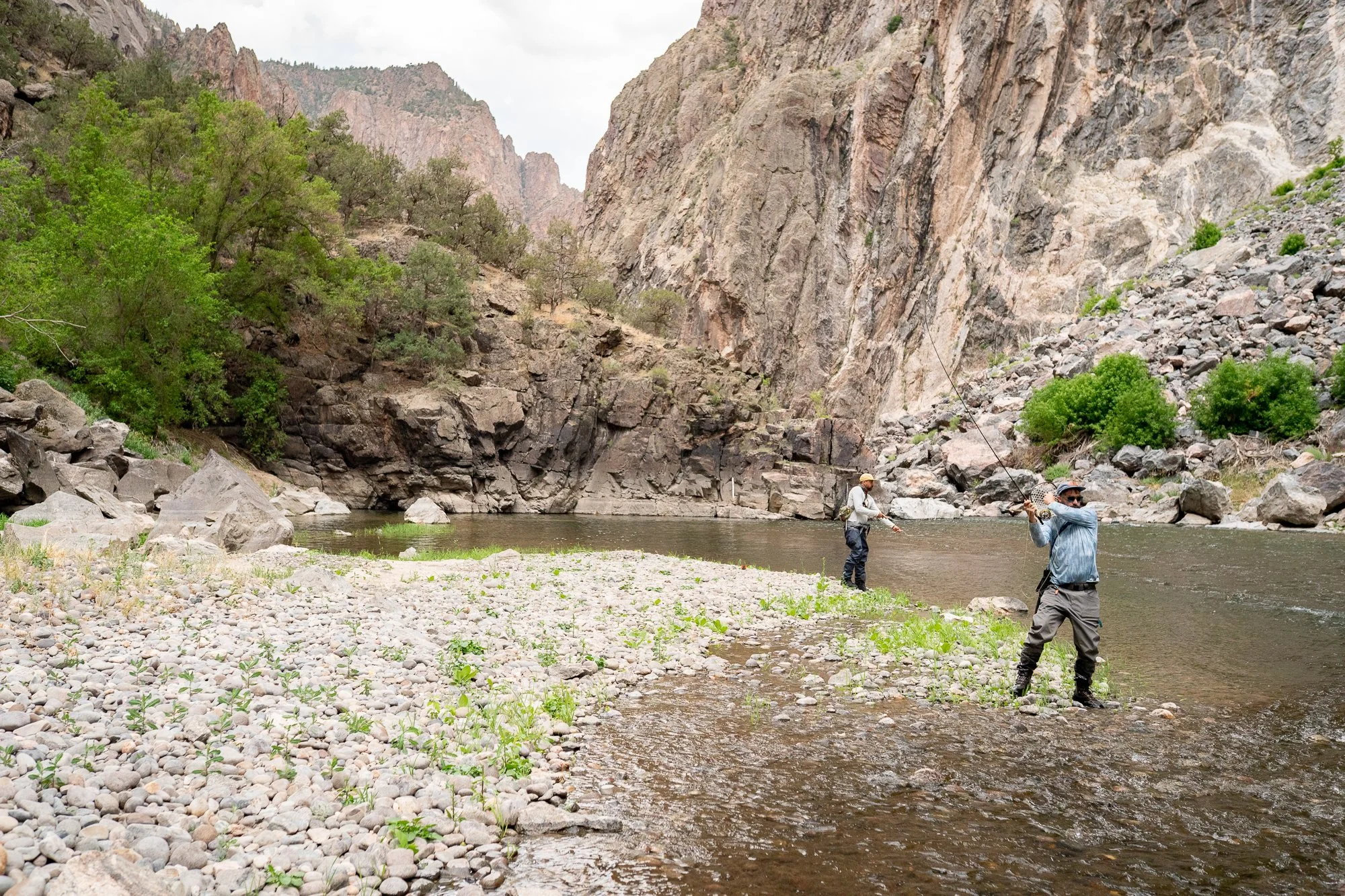 Two anglers fish wide canyon water beneath steep Black Canyon walls