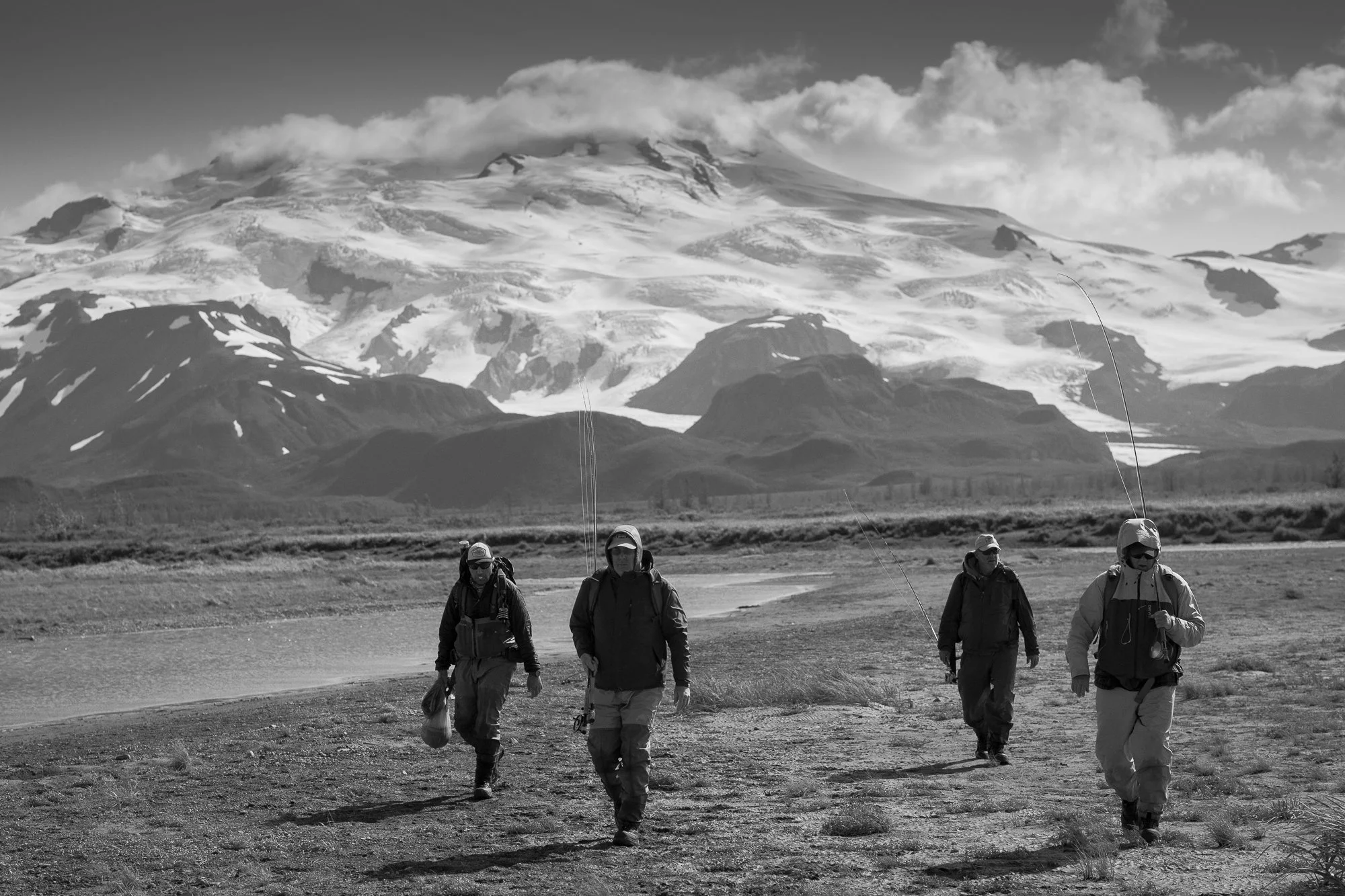 Four fly fishermen walking across a river with a mountain behind them
