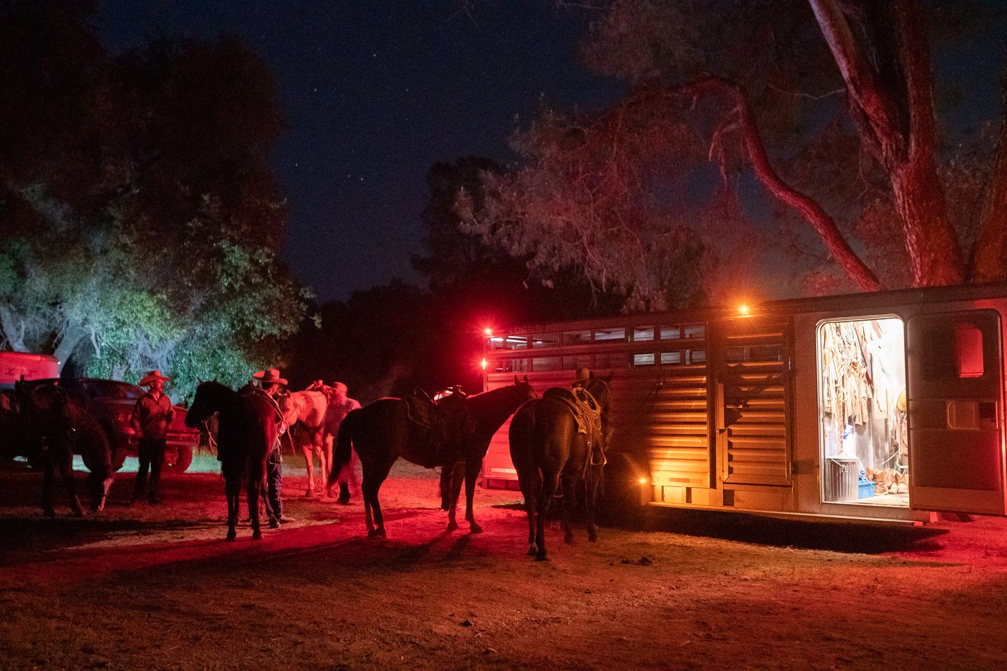 Cowboys and horses gathered near trailer at night illuminated by red and warm lights