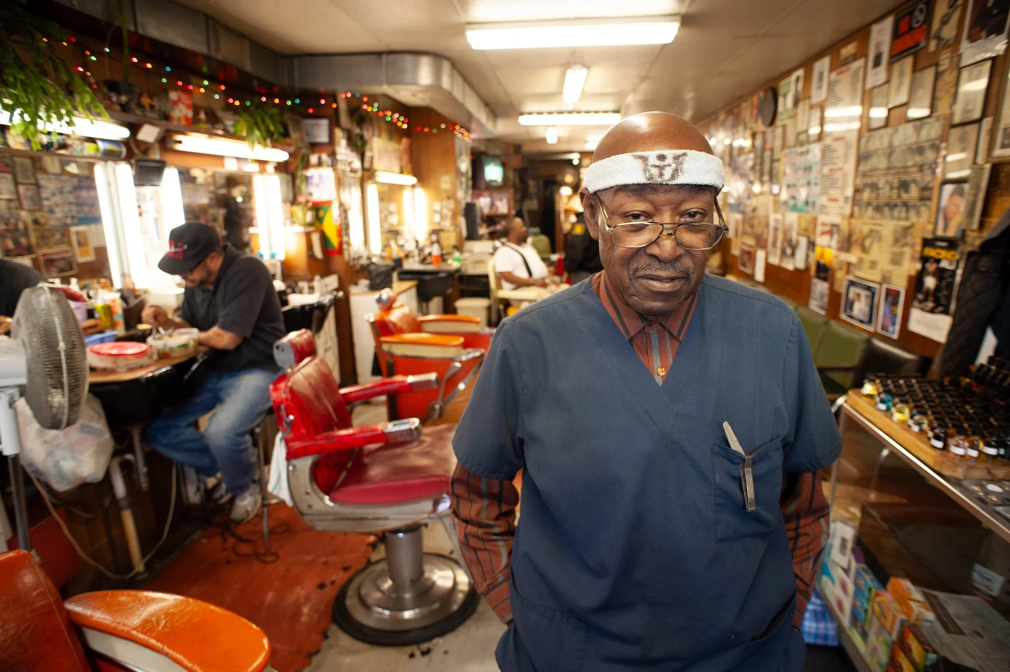 Portrait of a barber standing inside a traditional Black barbershop with chairs and mirrors behind him