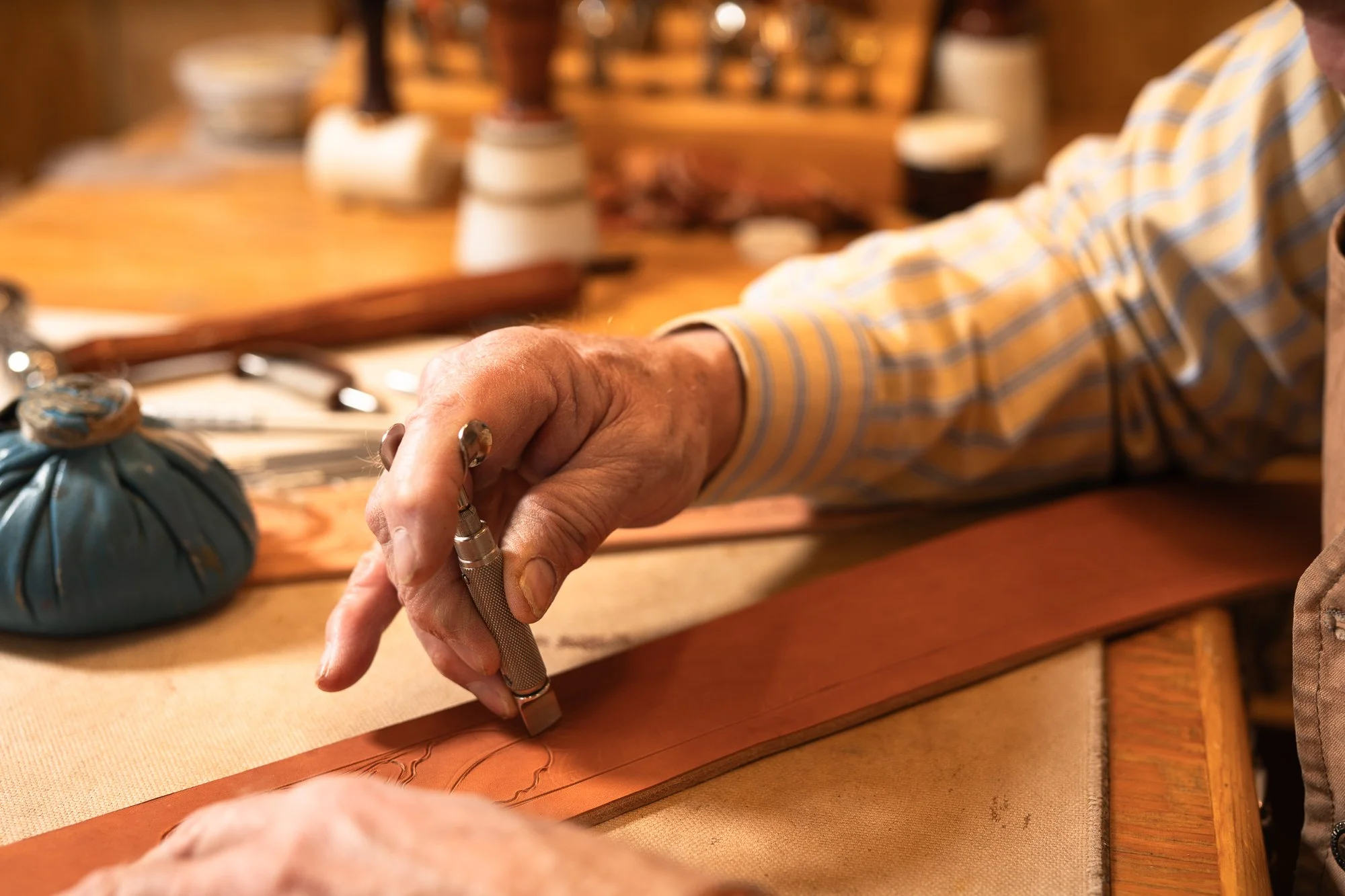 Western saddle maker carving leather by hand at a workbench