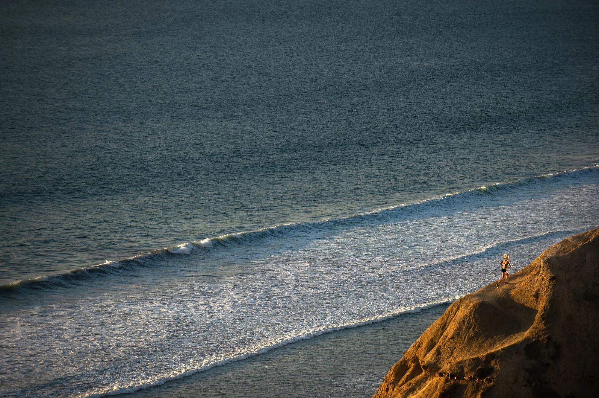 runner on coastal cliff trail overlooking ocean during workout