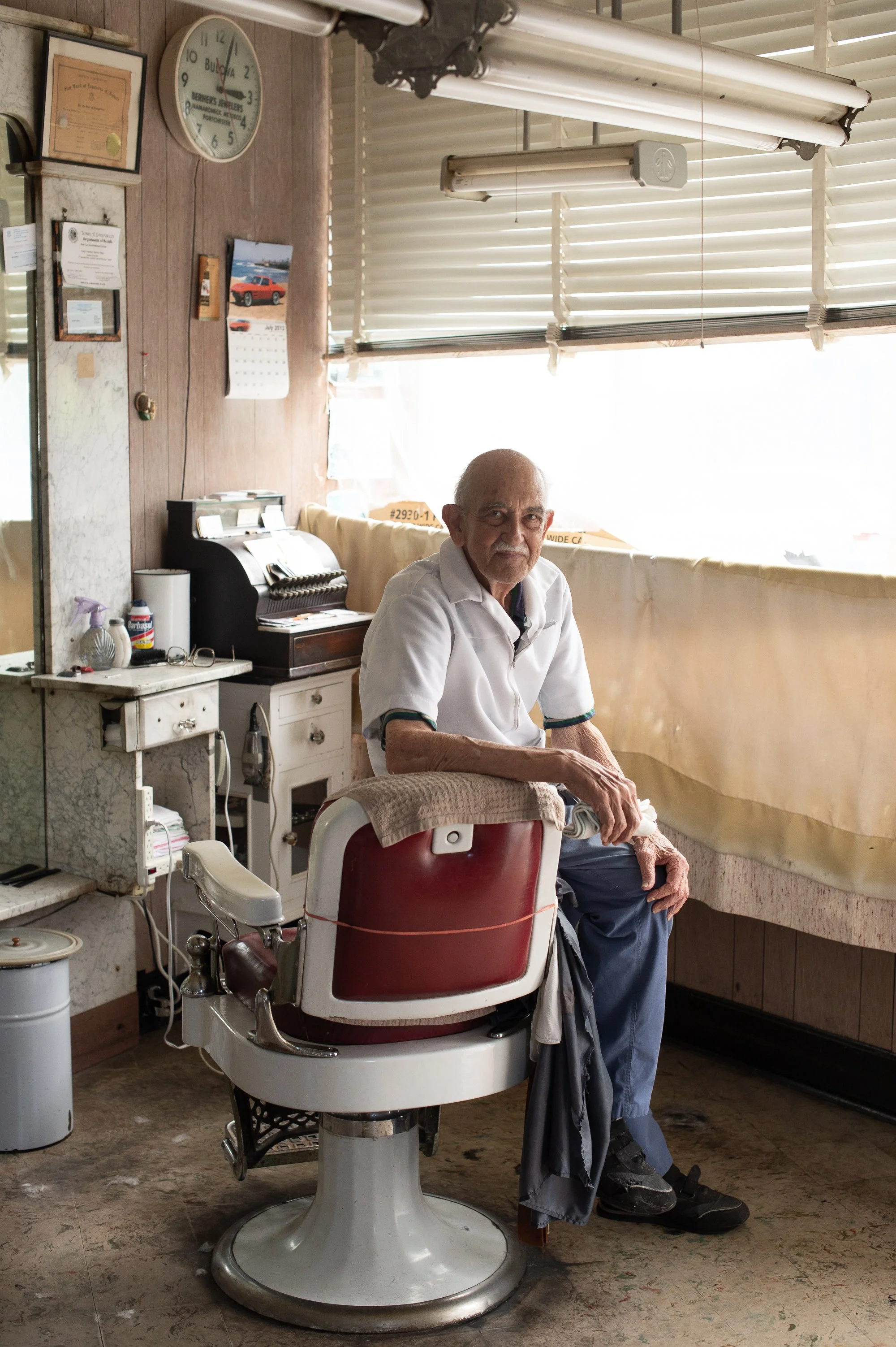 portrait of elderly barber Tony sitting in barber chair inside his Greenwich Connecticut shop