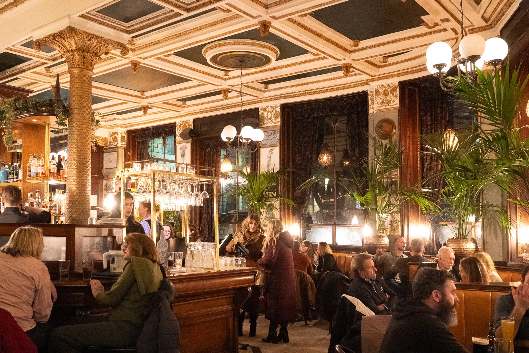 Wide interior view of Cafe Royal in Edinburgh with ornate ceiling, carved columns, and evening crowd