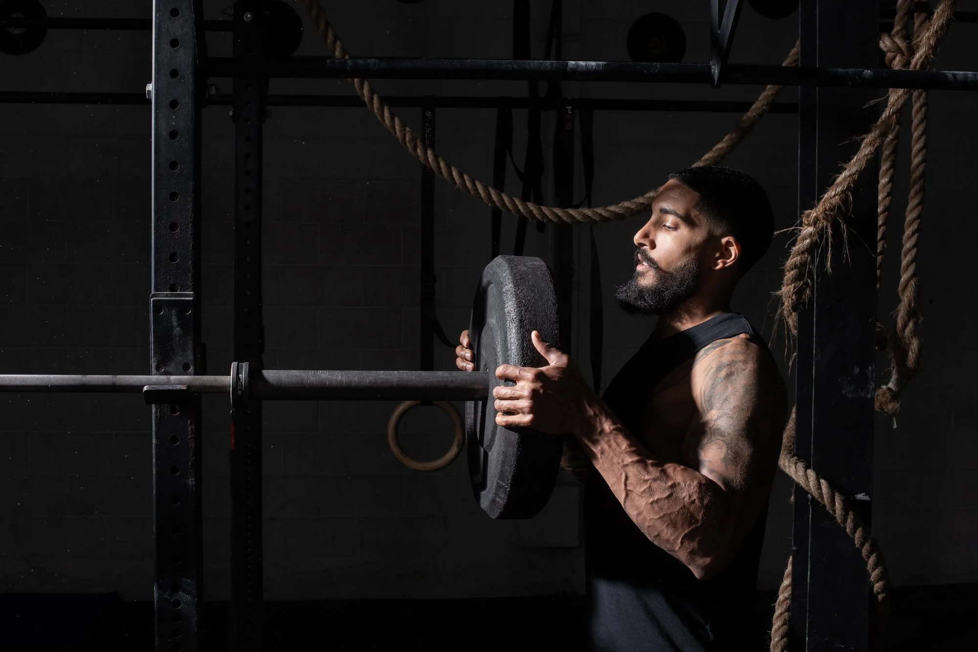 Athlete loads a weight plate onto a barbell in a Colorado gym, surrounded by ropes and  strength equipment