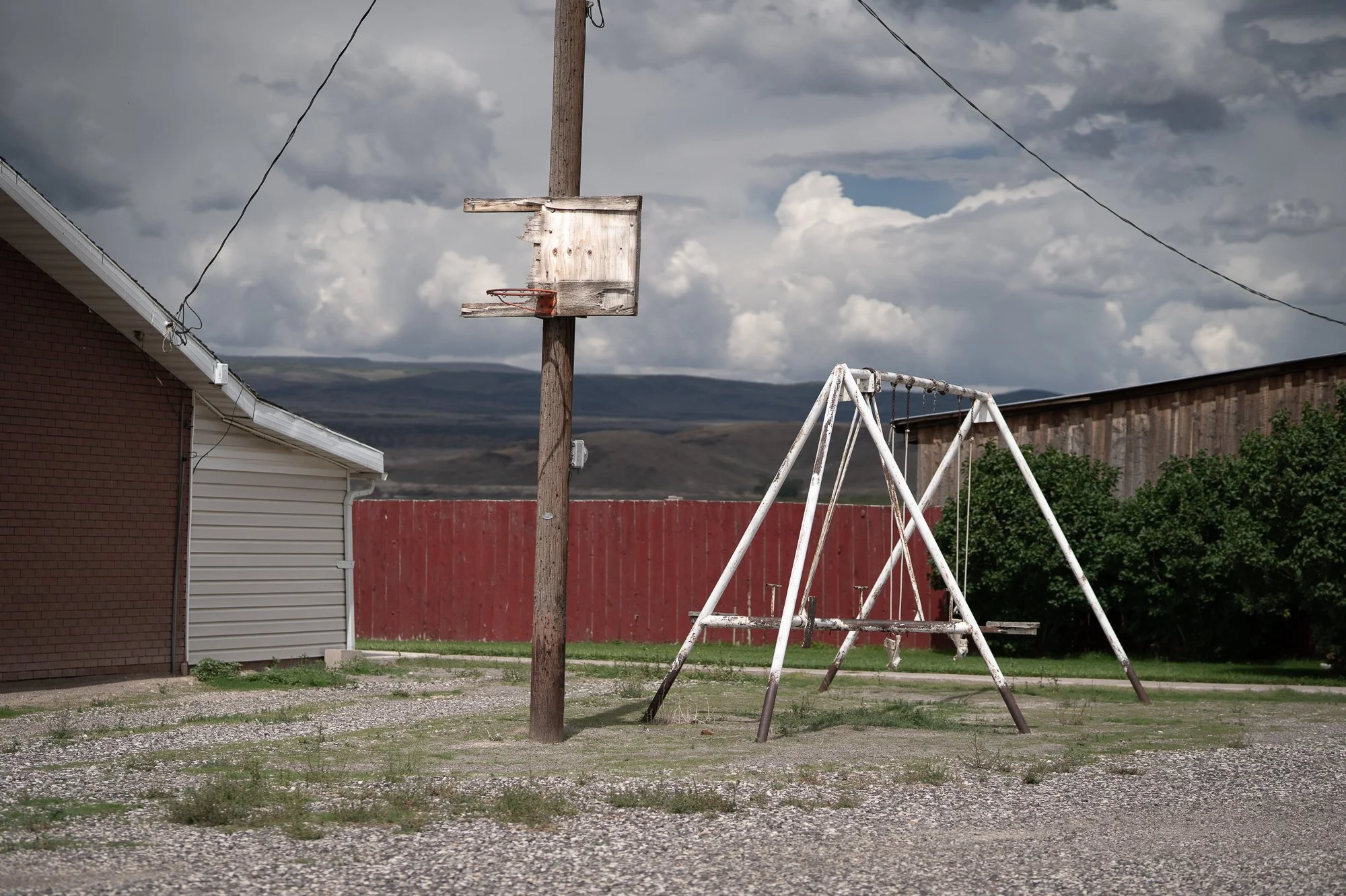 Weathered basketball hoop beside a swing set under a cloudy sky