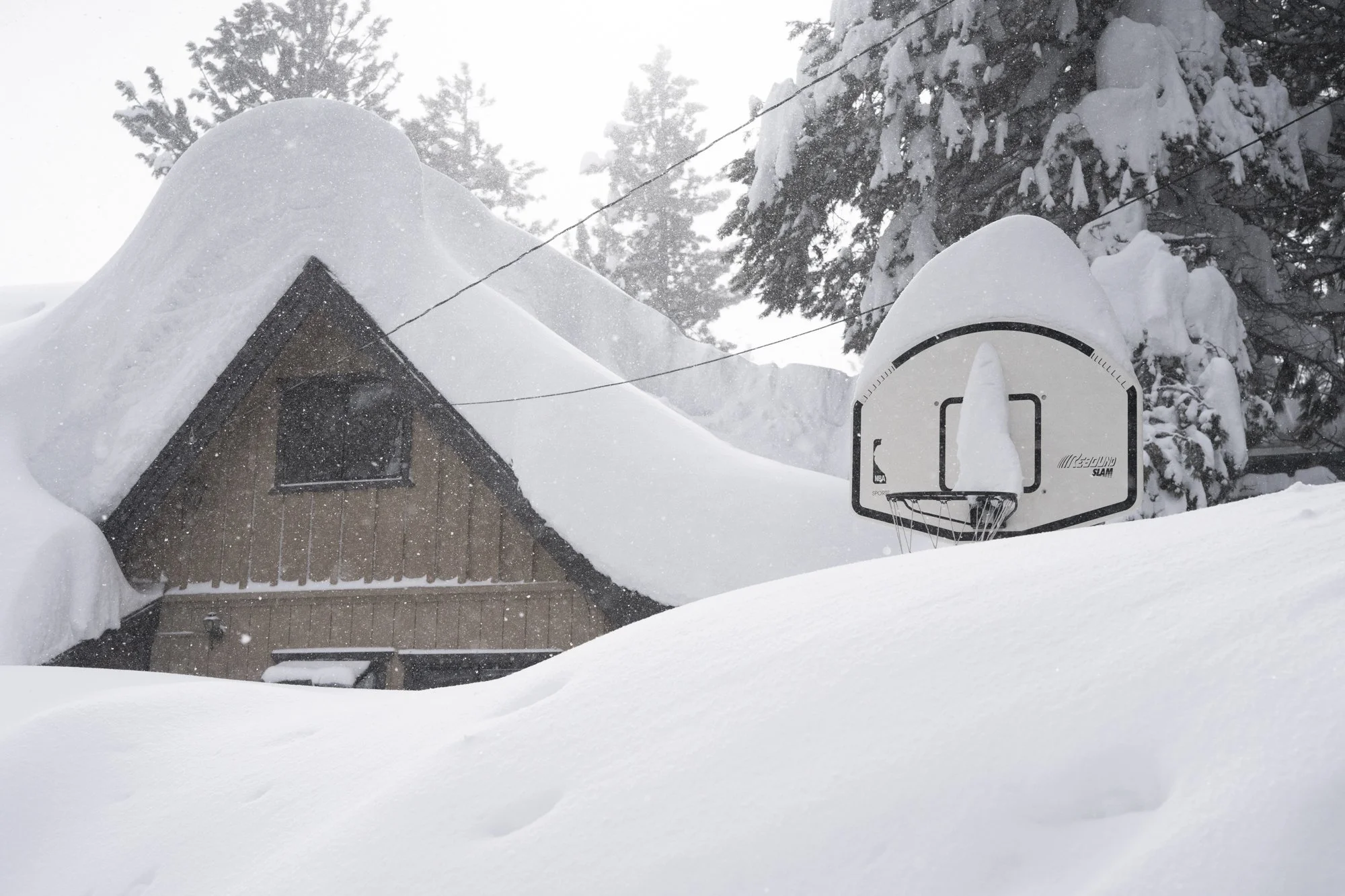 A basketball hoop and cabin covered in fresh snow after a winter storm