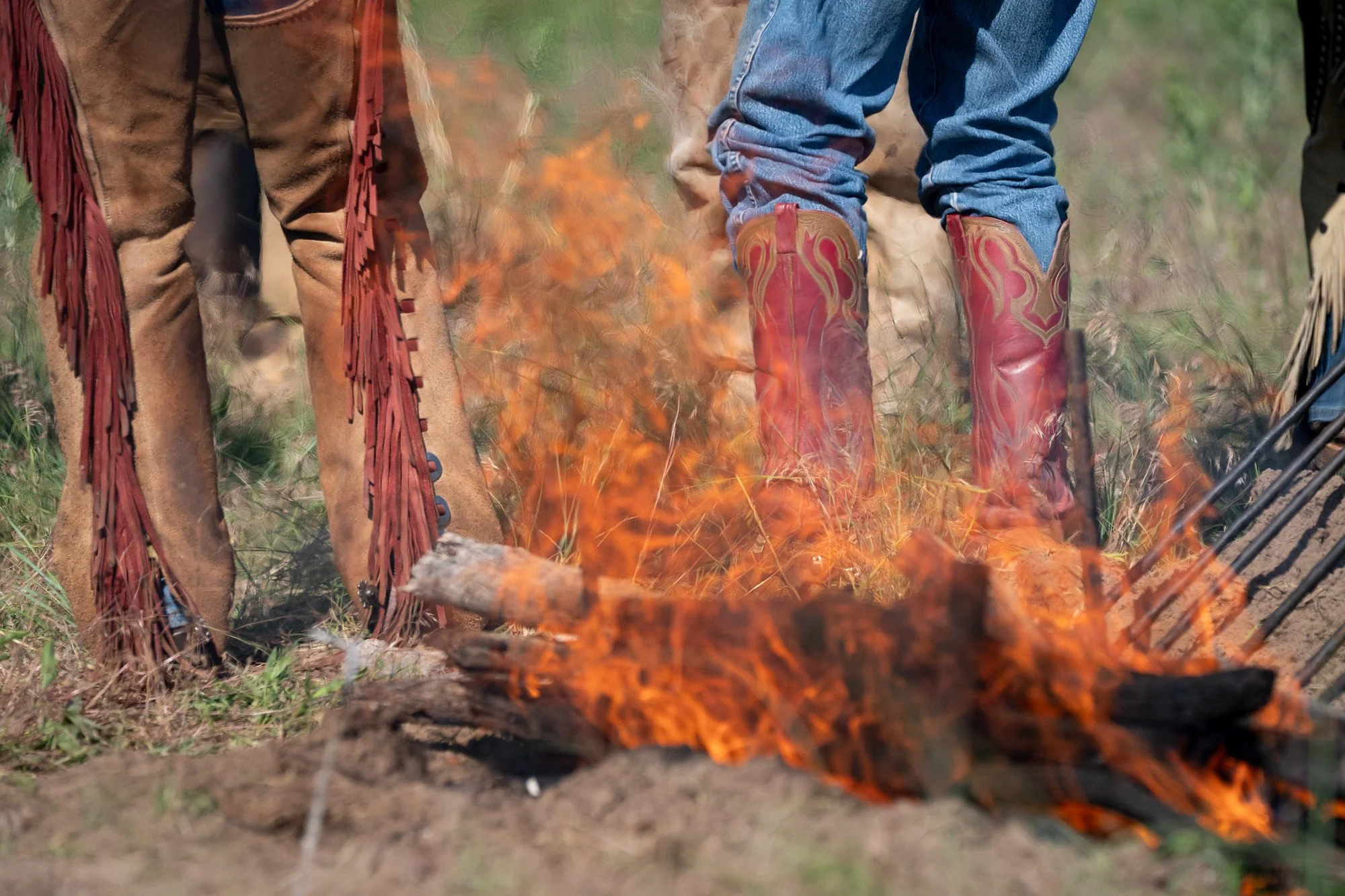 Cowboy boots and chaps standing near open fire during ranch work or camp
