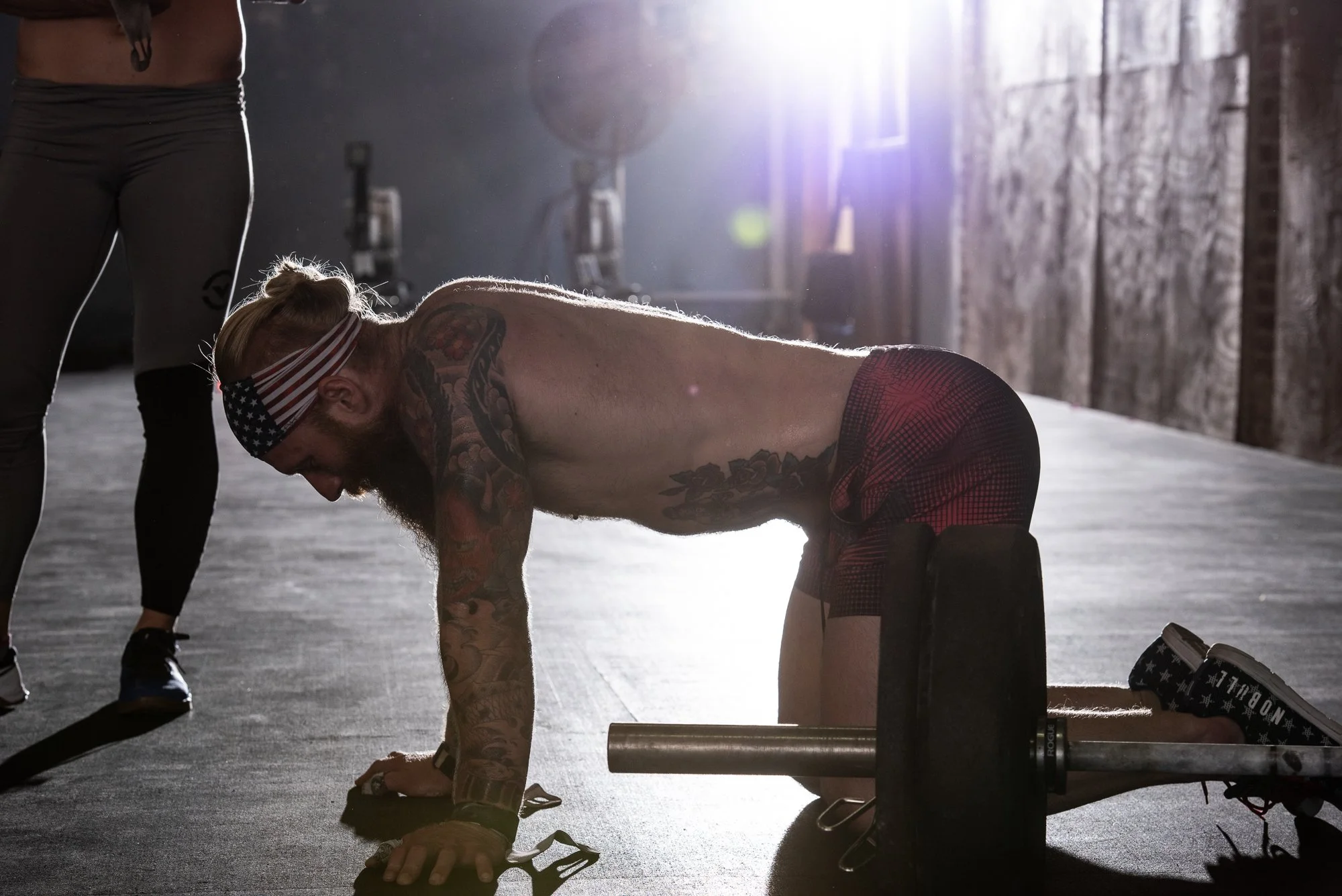 CrossFit athlete working beside a loaded barbell on the gym floor.