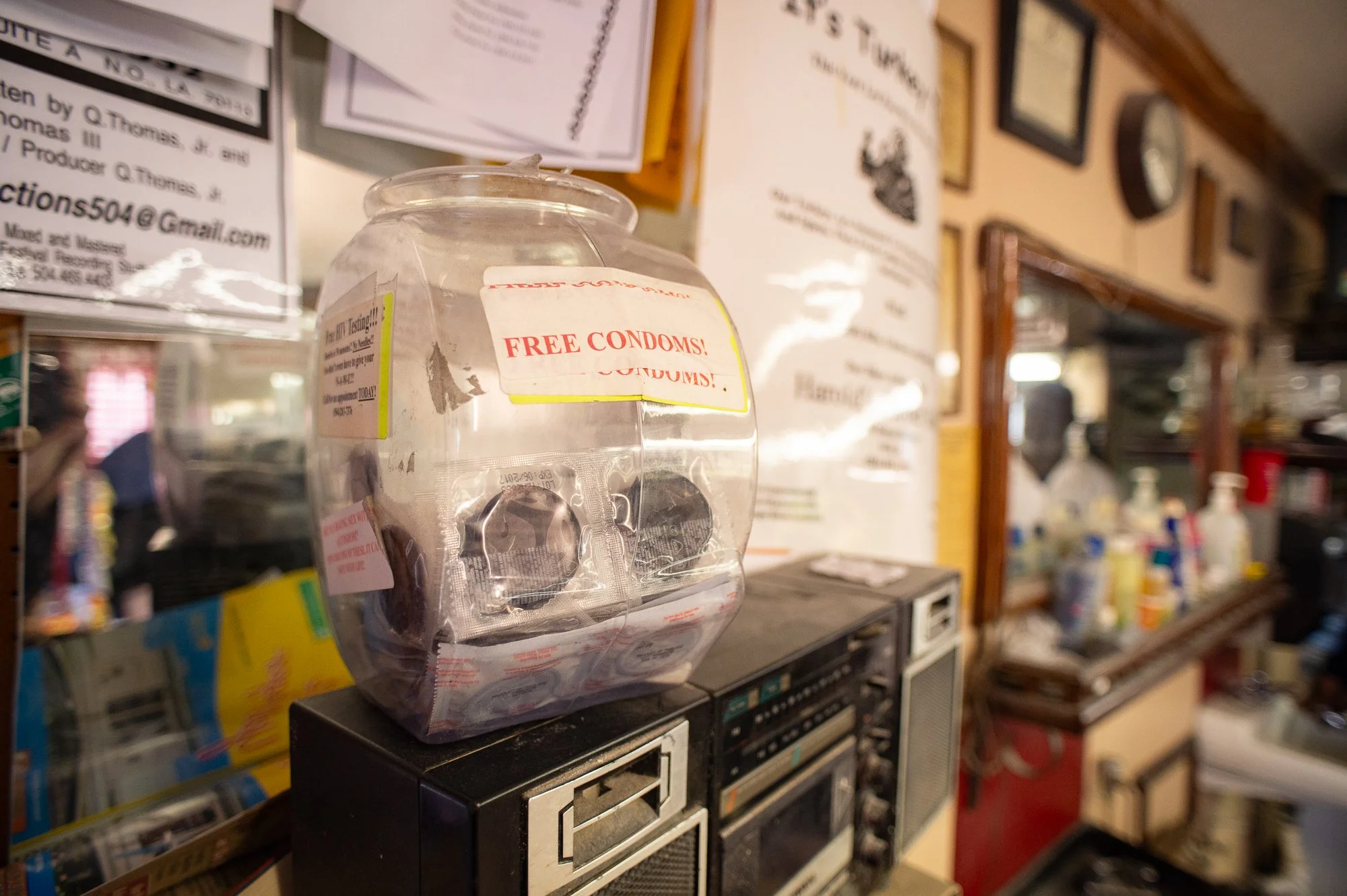 Jar labeled free condoms sitting on a counter inside a Black barbershop with posters behind it