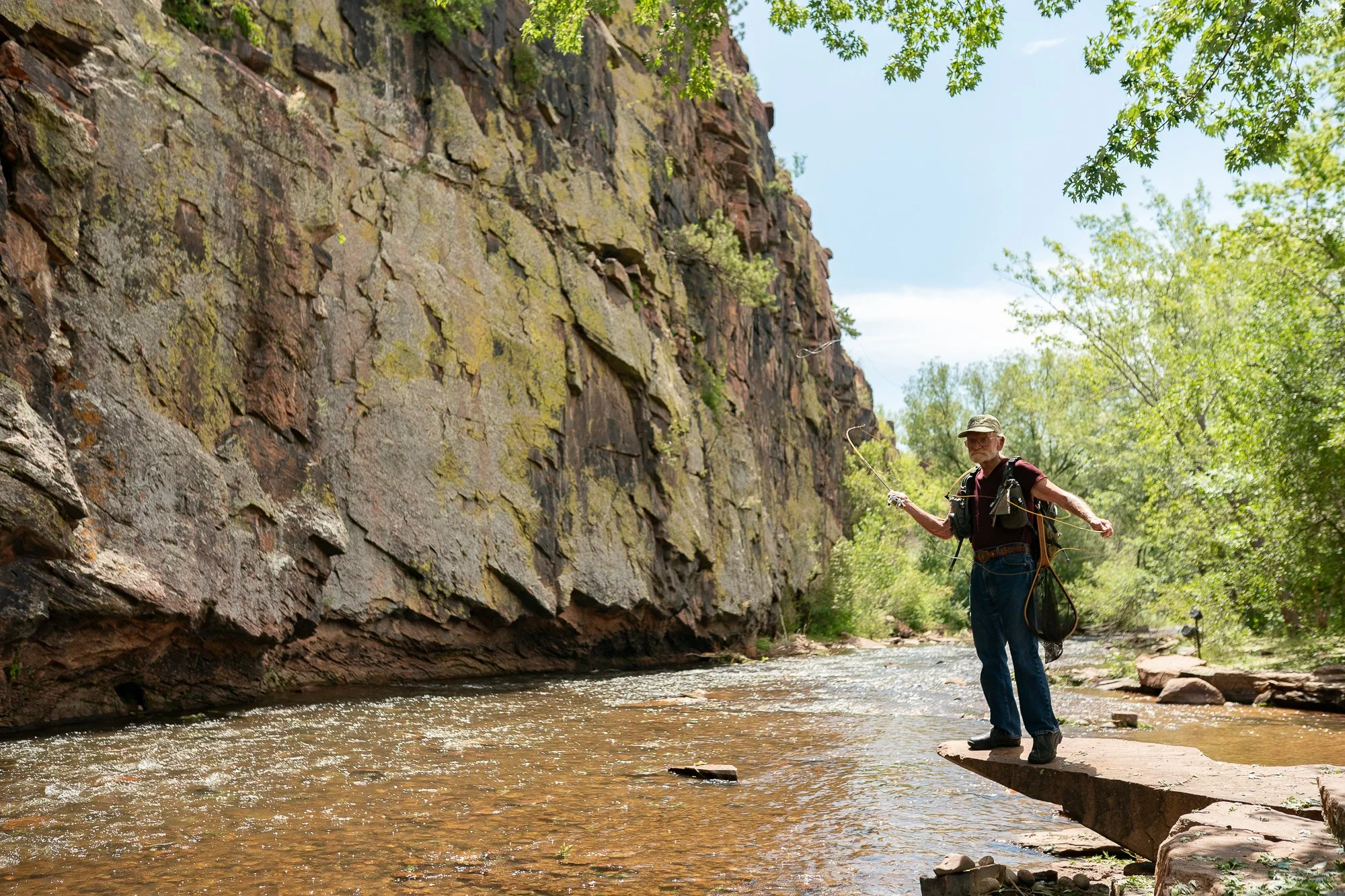 Mike Clark fly fishing with a bamboo rod beside a rocky canyon wall in Colorado.