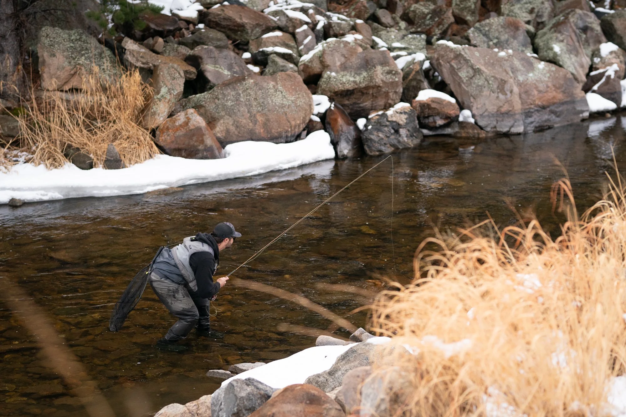Photograph of a fly fisherman crouching in the river to avoid being seen by fish