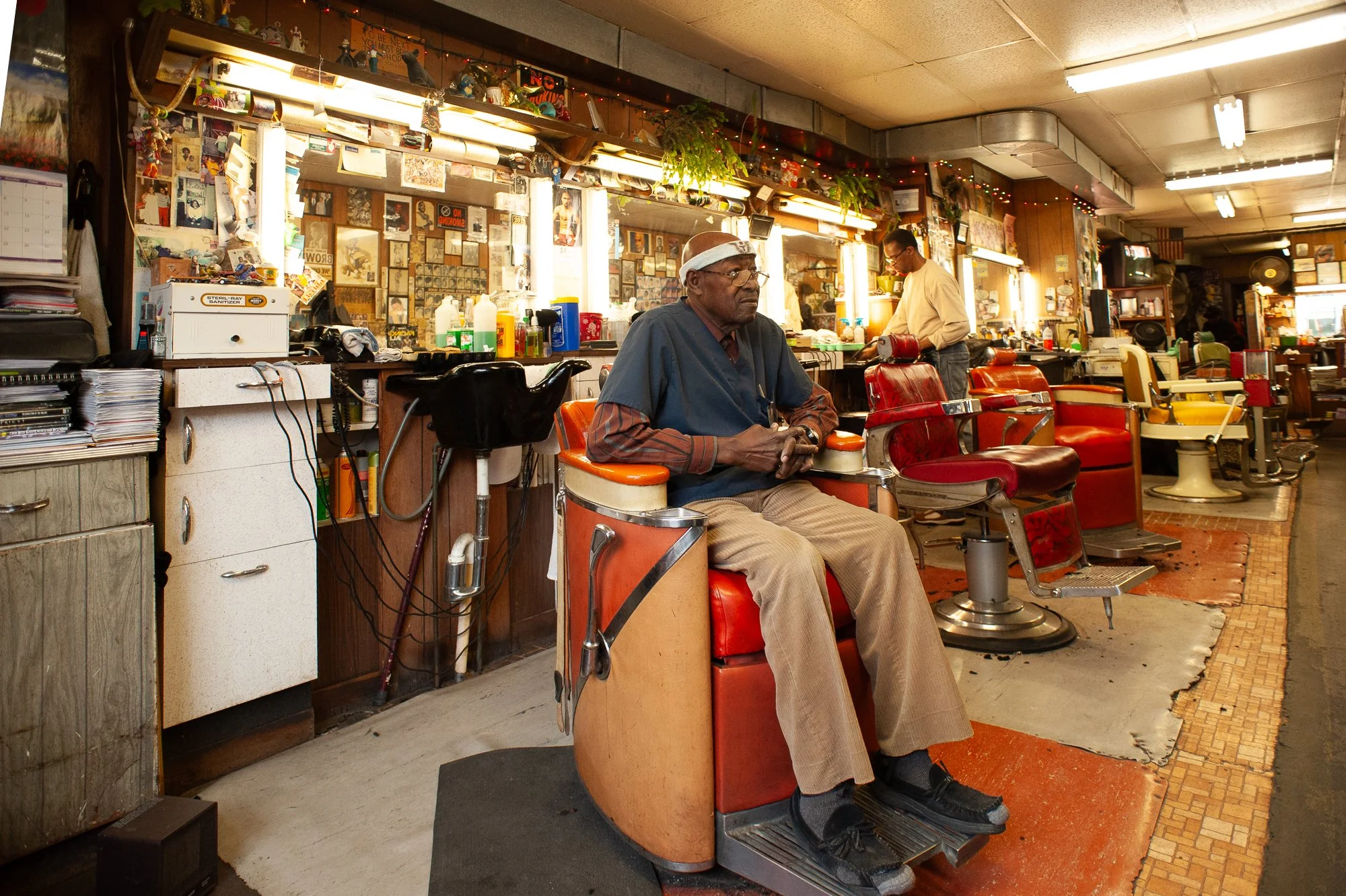 Barber seated inside Stancil’s Barbershop Albany NY, traditional Black barbershop interior photographed in 2011