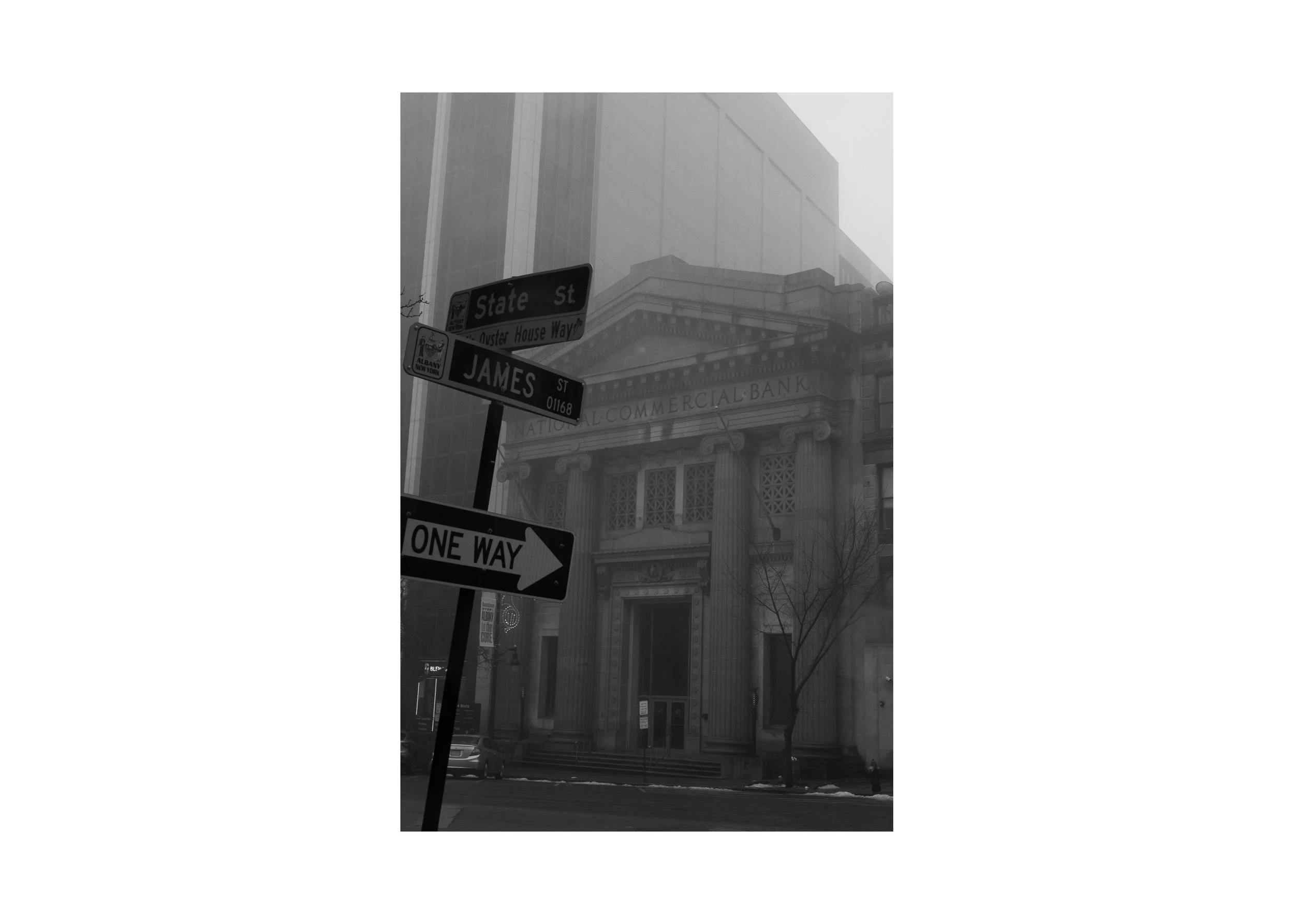 Black and white photograph of State and James Streets in Albany, New York, showing historic architecture and street signs in winter fog