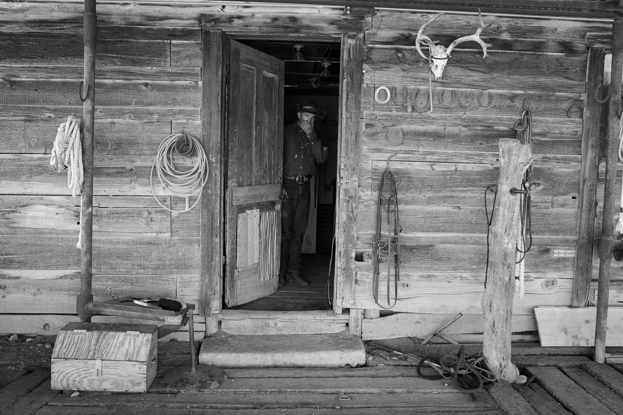 Cowboy standing inside a saddle house with ropes and tack on a working ranch