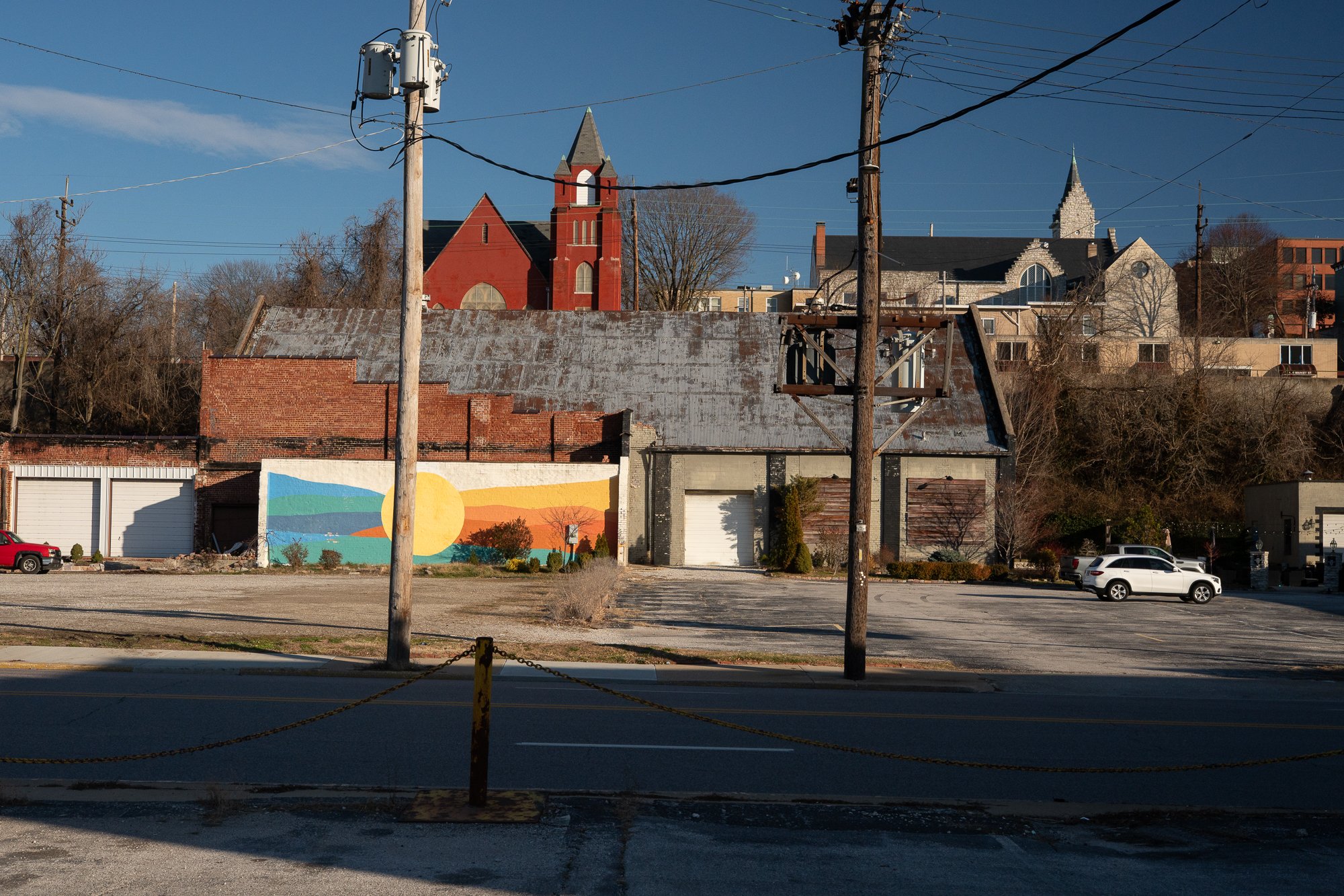 Colorful mural on a low building with industrial structures and an empty lot in Alton, Illinois