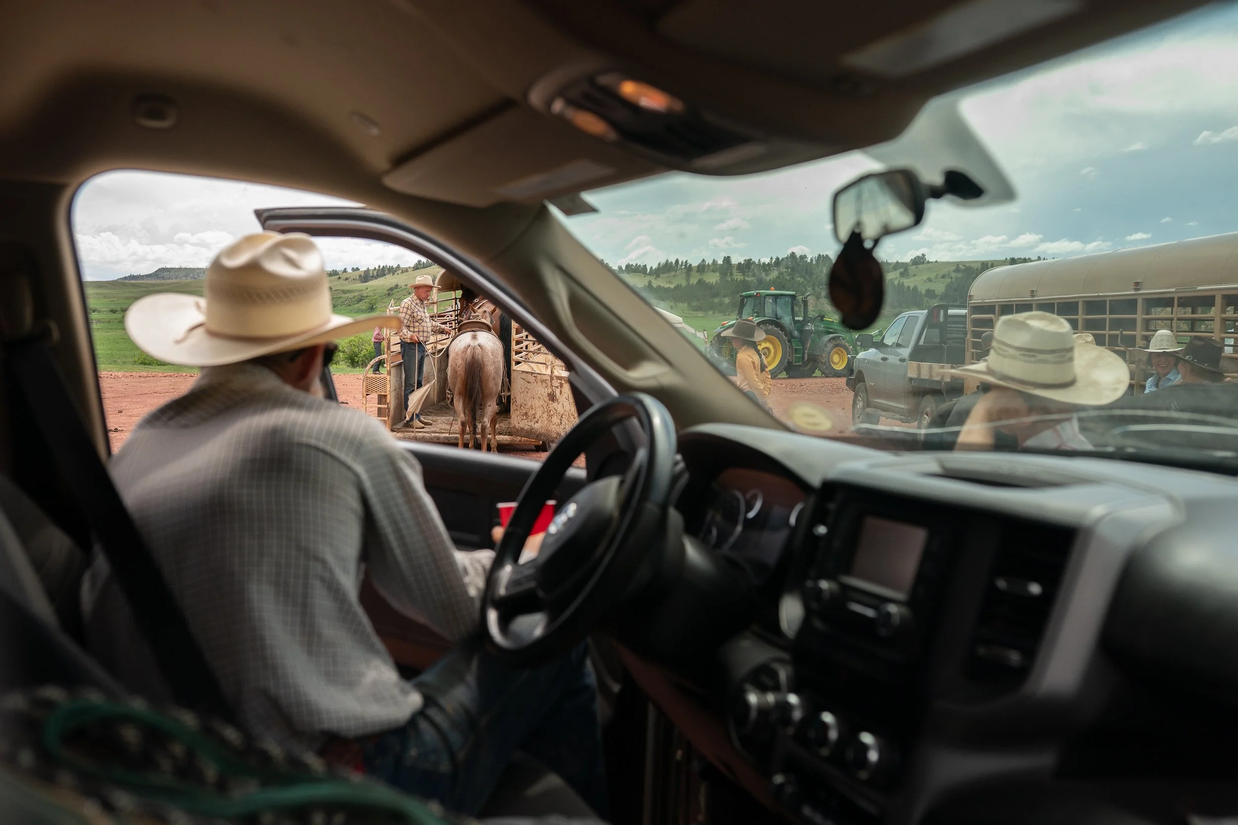 View from inside a pickup truck of a cowboy watching Buck Brannaman work a horse near trailers on a ranch