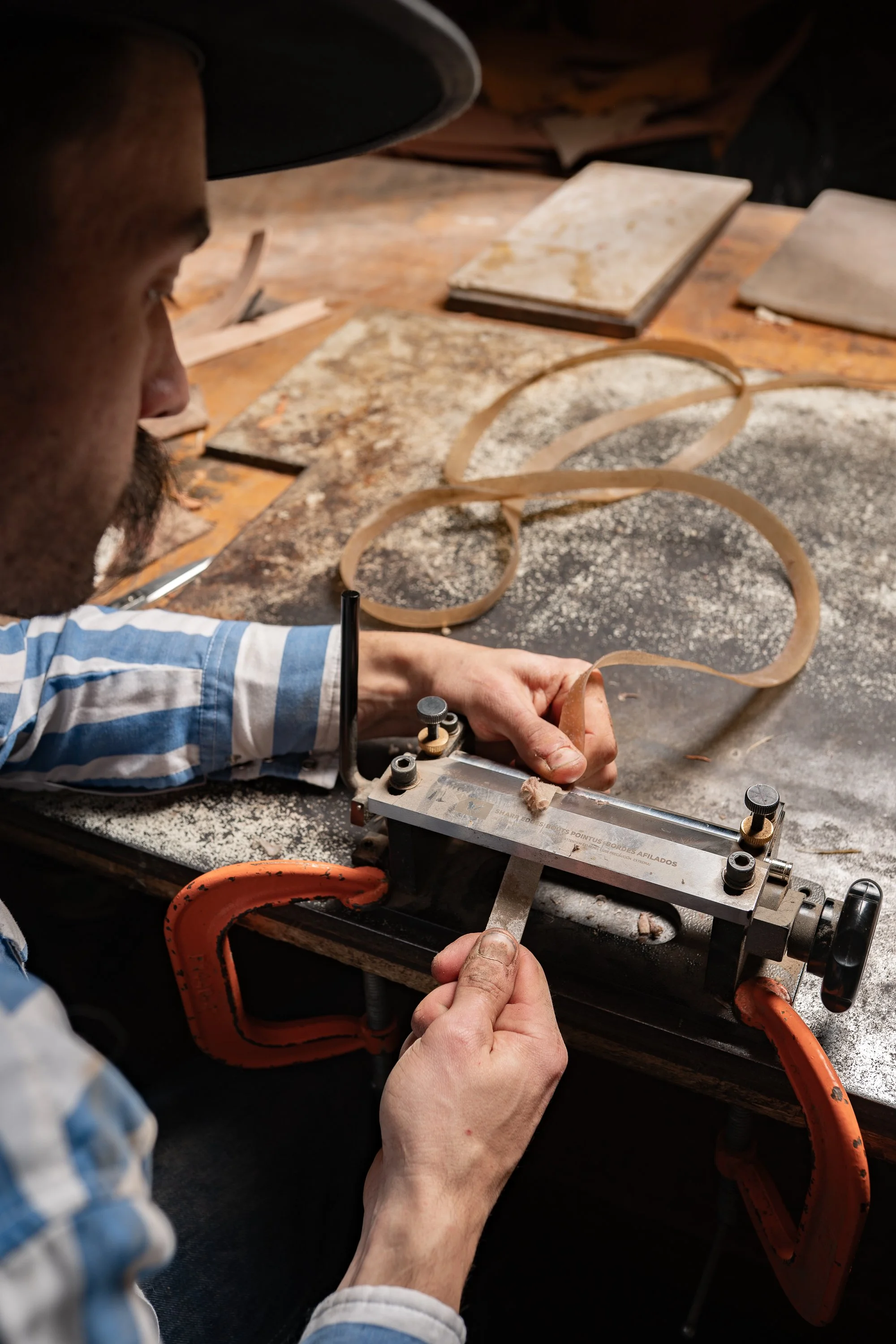 Dakota May using a beveling tool to shape a rawhide strand at his workbench before braiding
