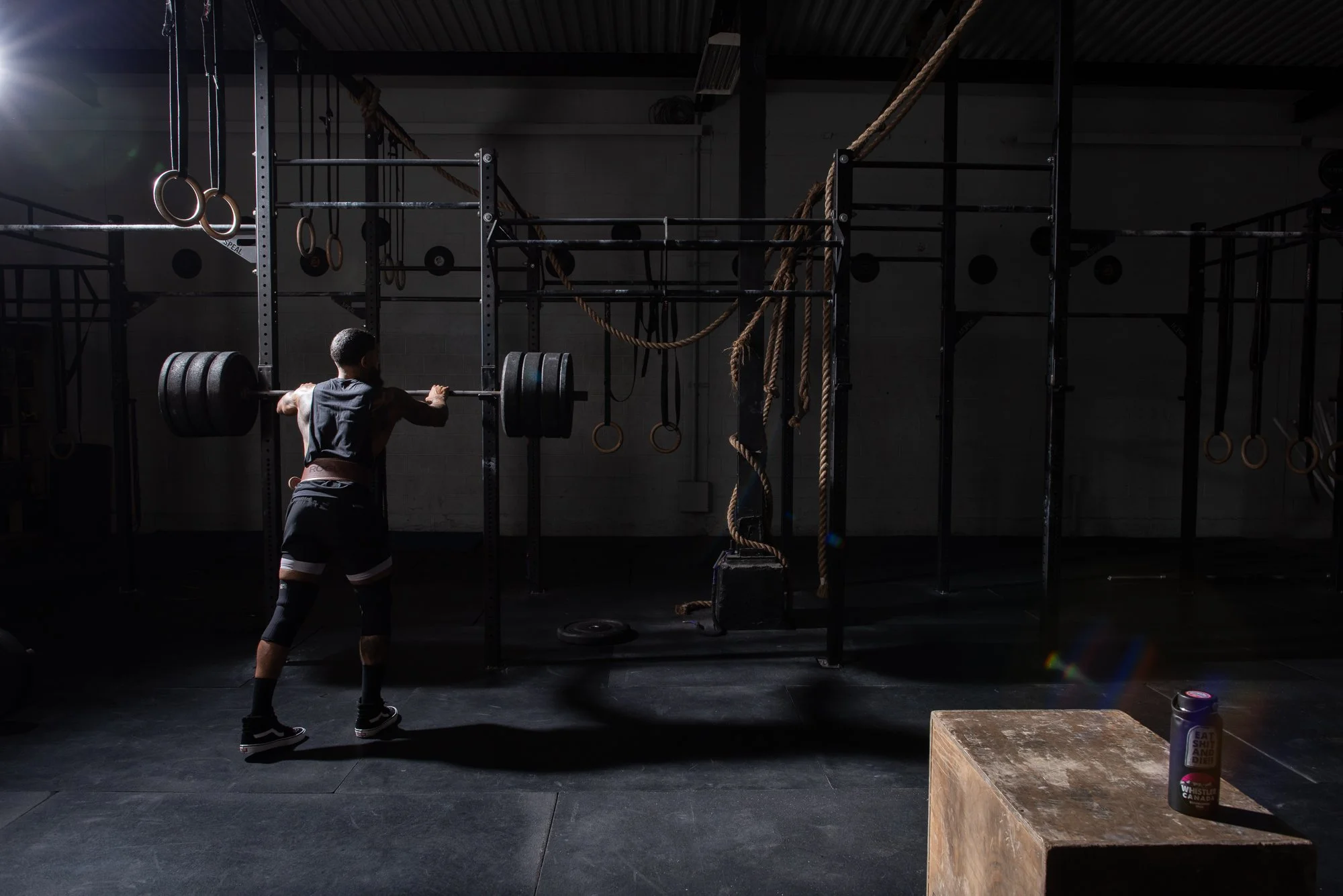 Athlete steps back from a barbell setup in a Colorado gym, surrounded by racks and ropes