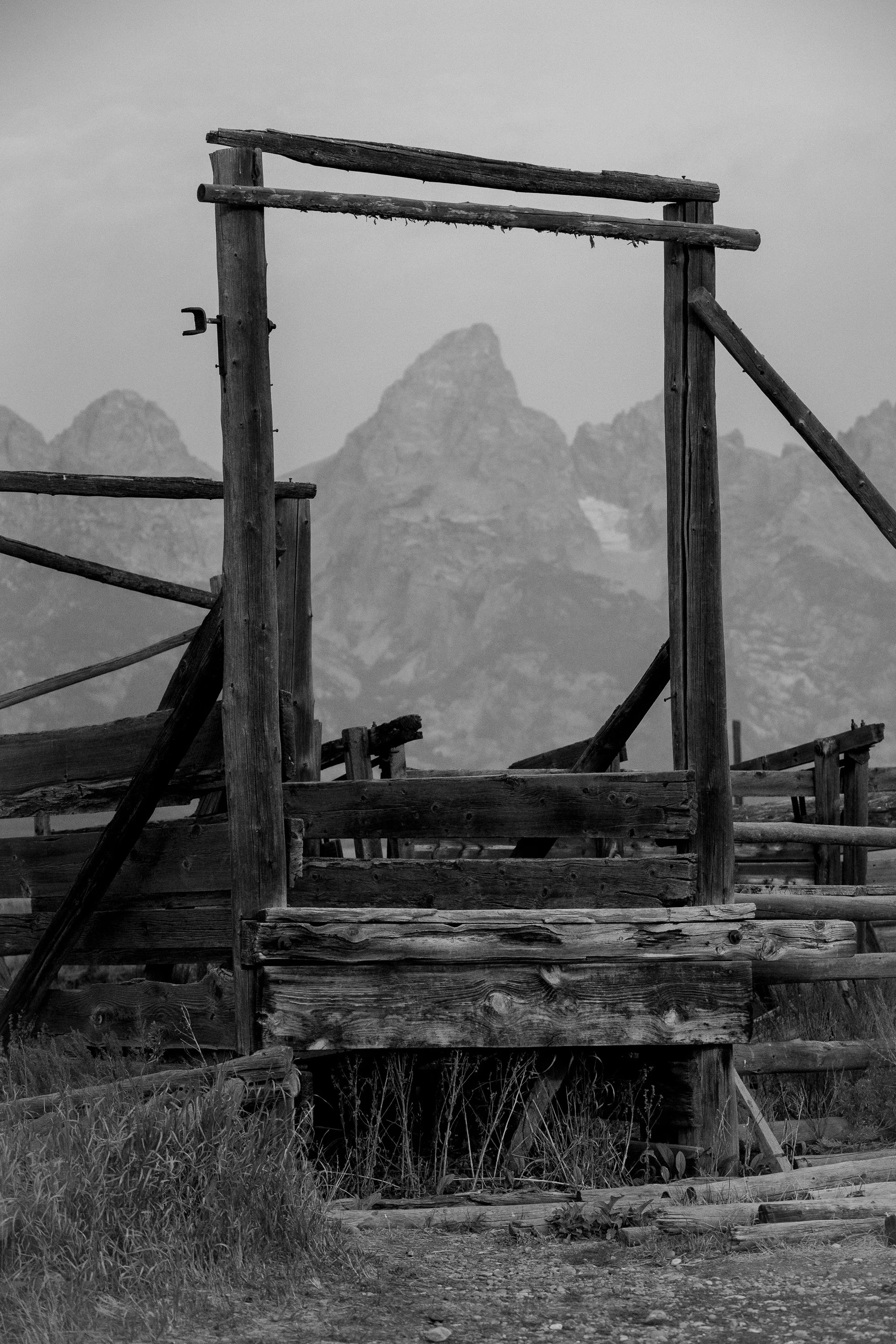 Black and white fine art photograph of the a wood cattle corral with the Grand Tetons in the background