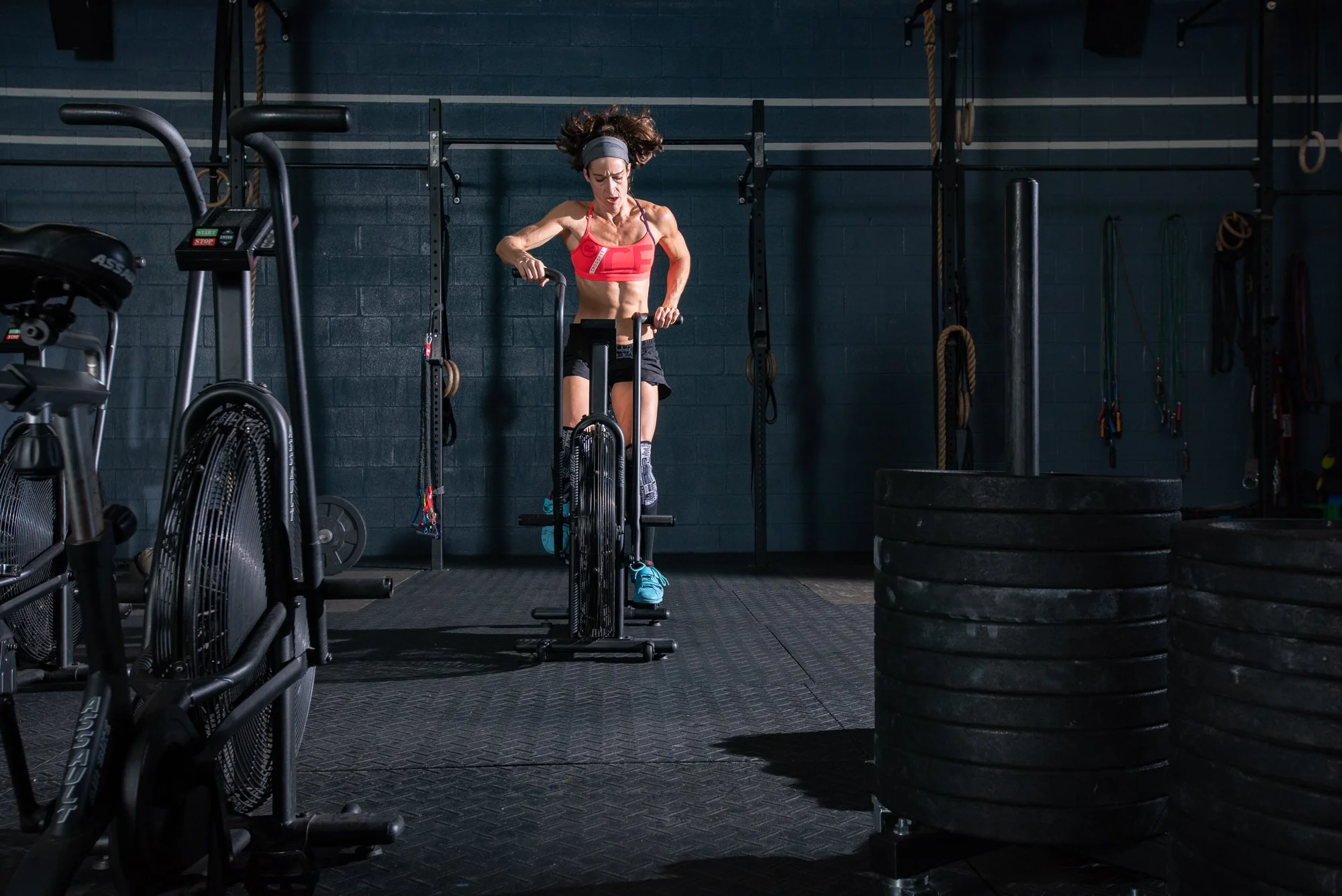 Female athlete using assault bike in crossfit gym during conditioning workout photoshoot