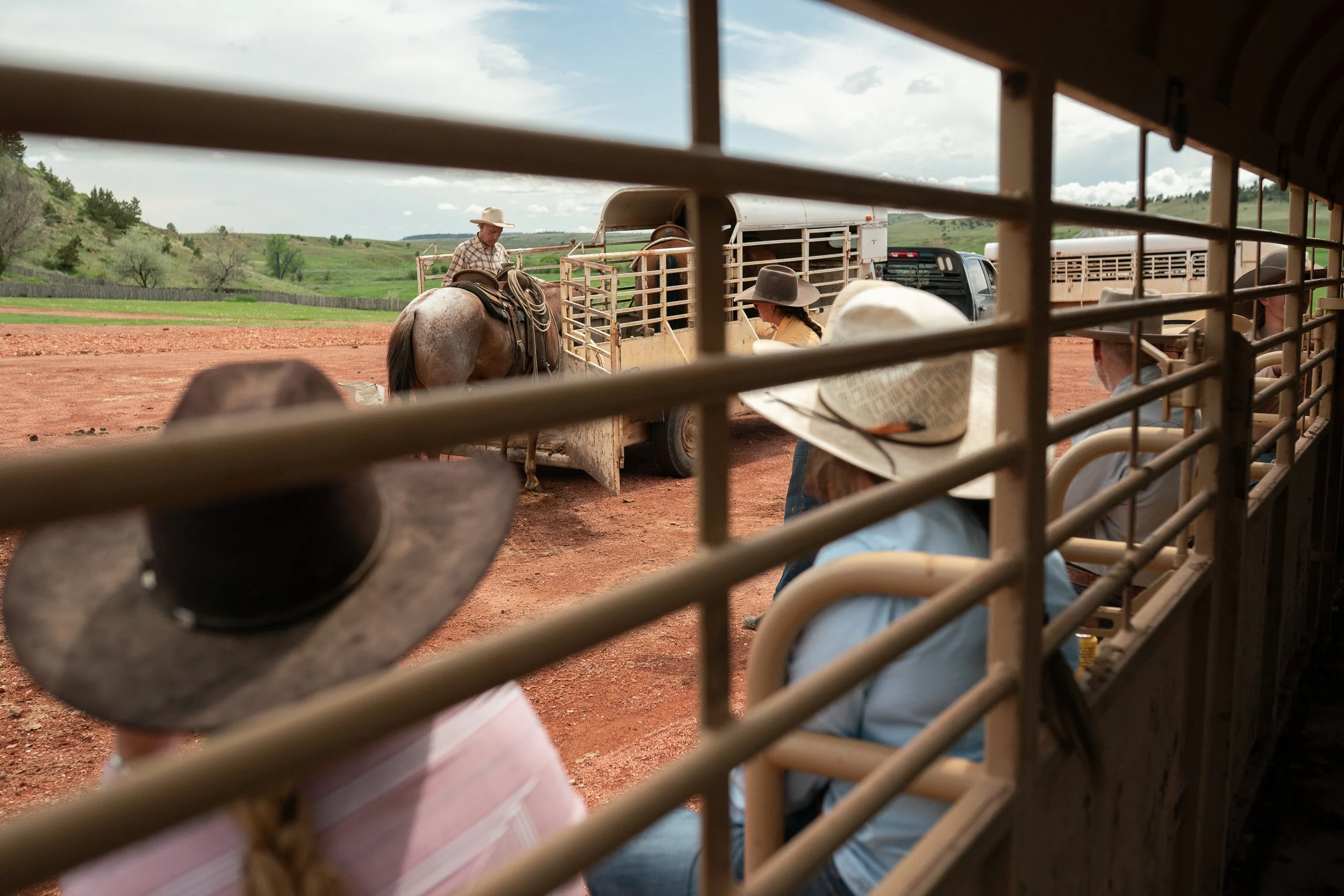 Cowboys watching through the rails of a trailer as Buck Brannaman works a horse near another trailer in Montana