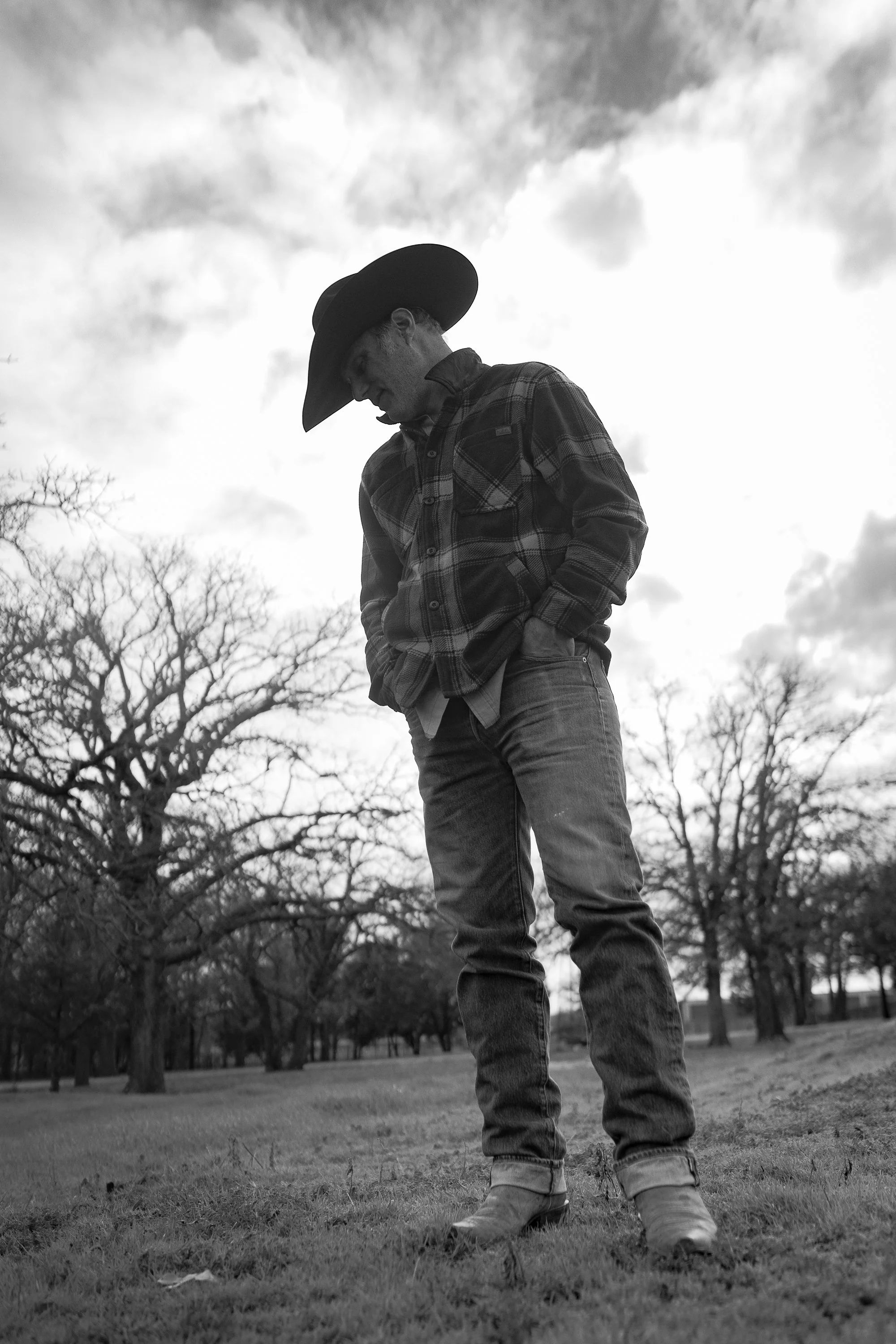 Black and white portrait of Western artist Teal Blake standing in a Texas field wearing a cowboy hat