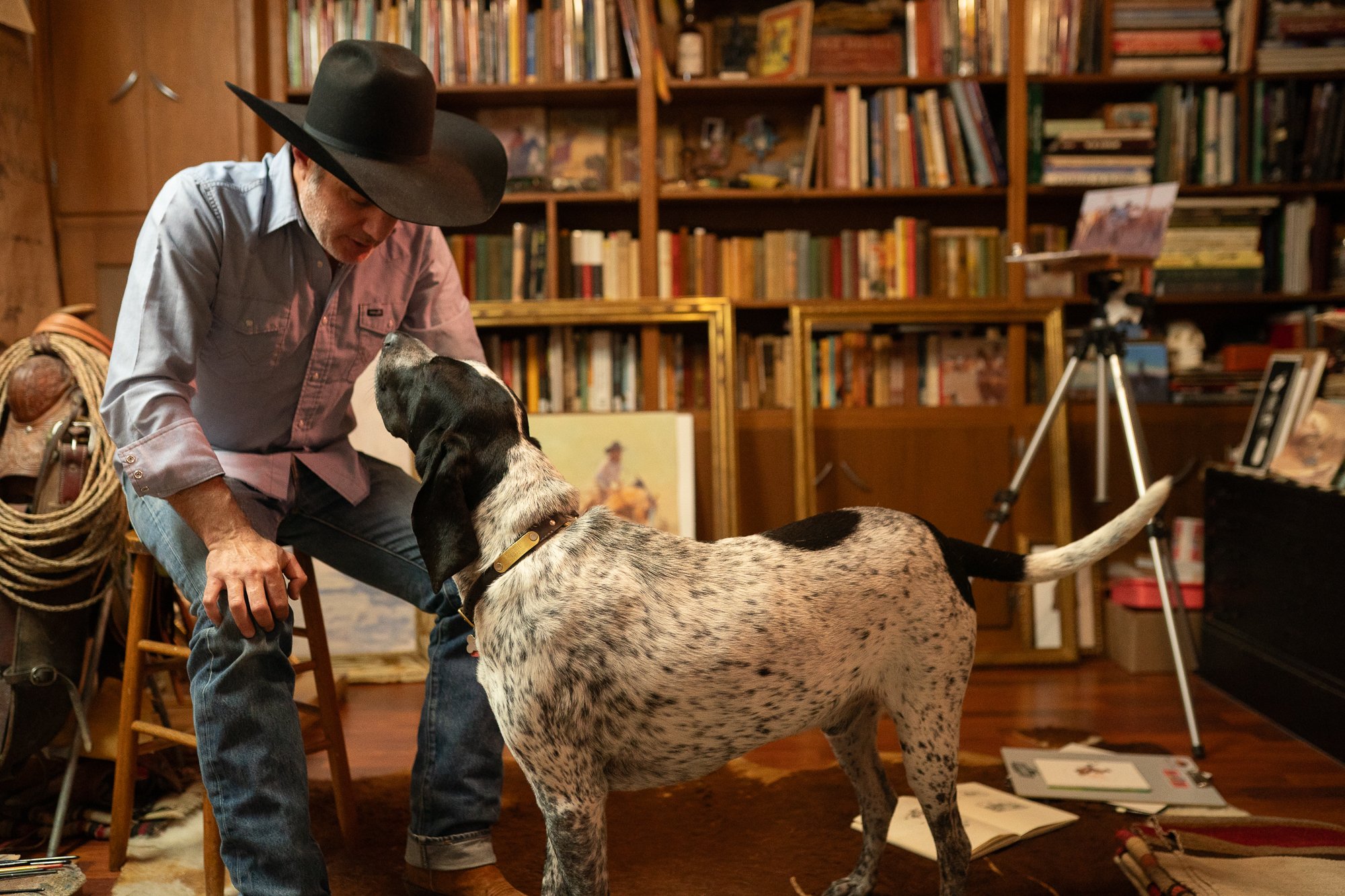 Western artist Teal Blake kneeling with his dog inside his Texas art studio