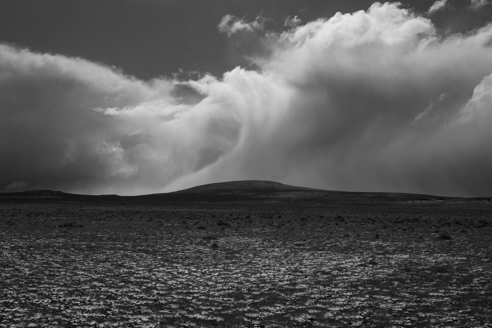 A black and white view of storm clouds over open high desert ranch land in Oregon