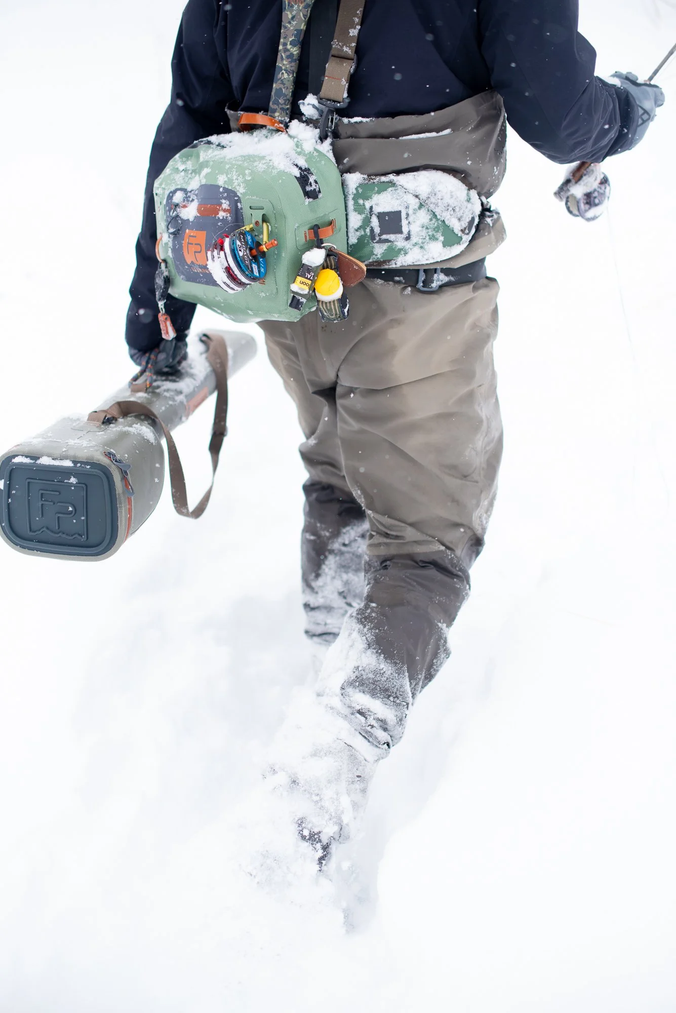 A close-up of fishing gear and pack covered in snow during winter fly fishing on Clear Creek in Colorado.