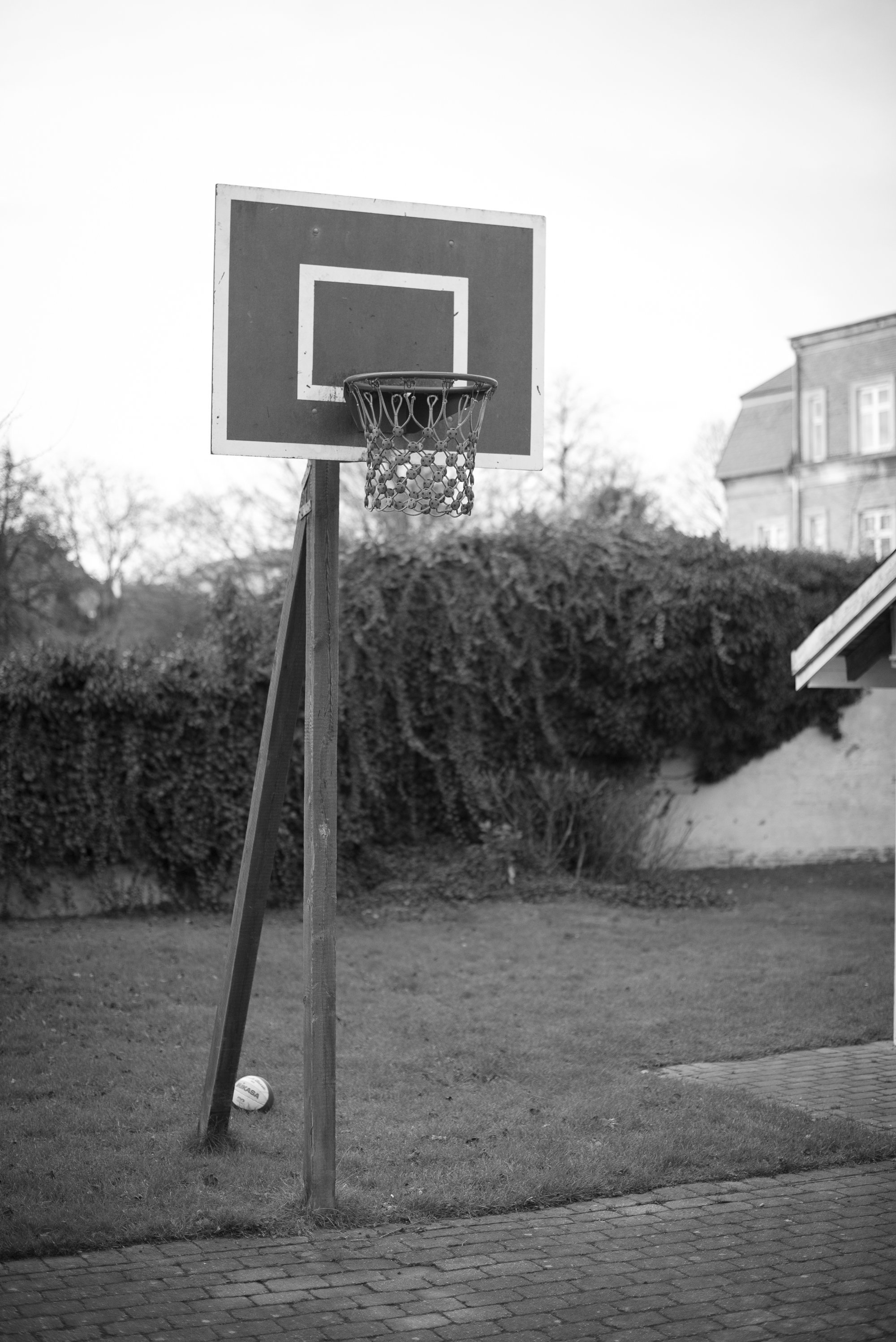 Black and white photograph of a residential basketball hoop set on a small outdoor court in Europe.