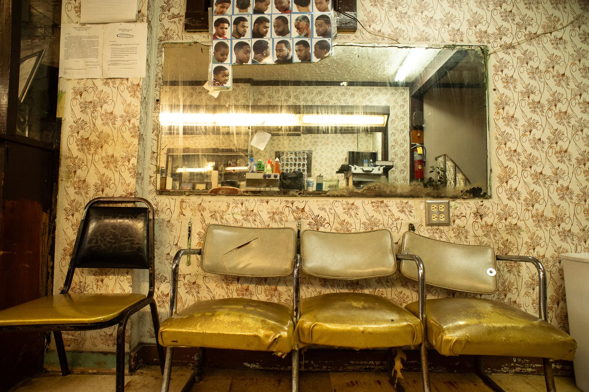 Old worn waiting chairs inside a historic barbershop with patterned wallpaper and mirror