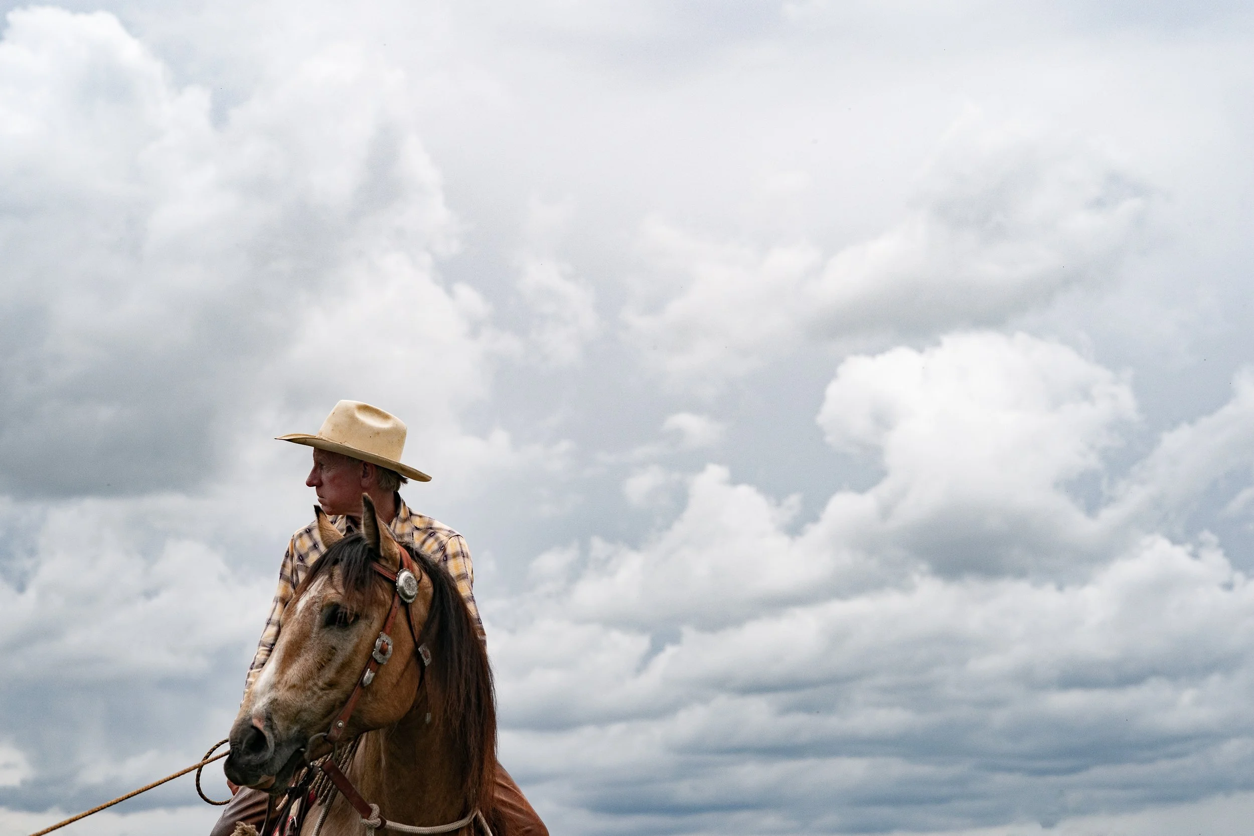 Cowboy sitting on a horse under a wide cloudy sky in Montana, looking off into the distance