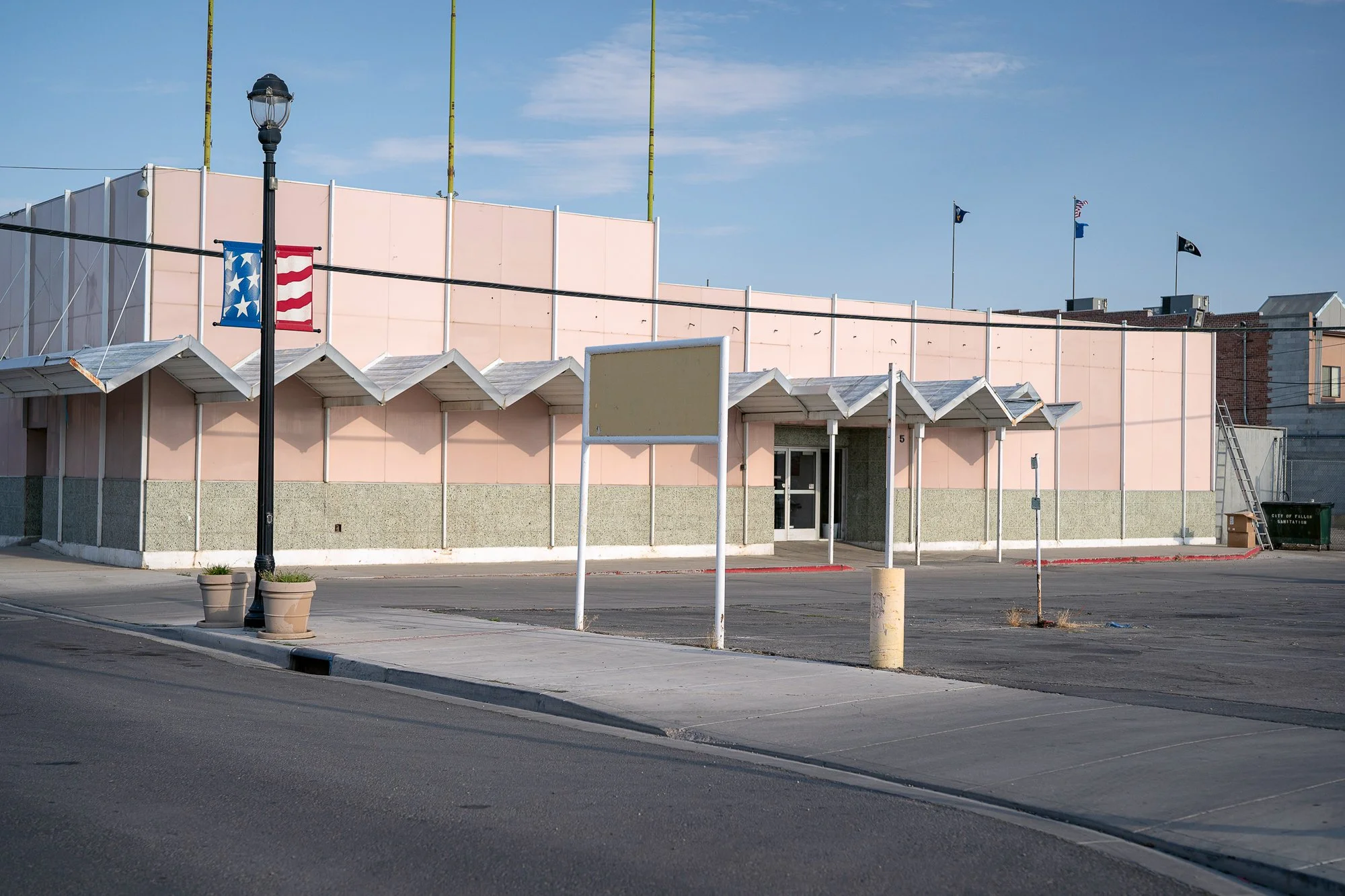 Vacant pink commercial building with zigzag canopy awnings, an empty sign frame, and a bare parking lot in a small Nevada town.