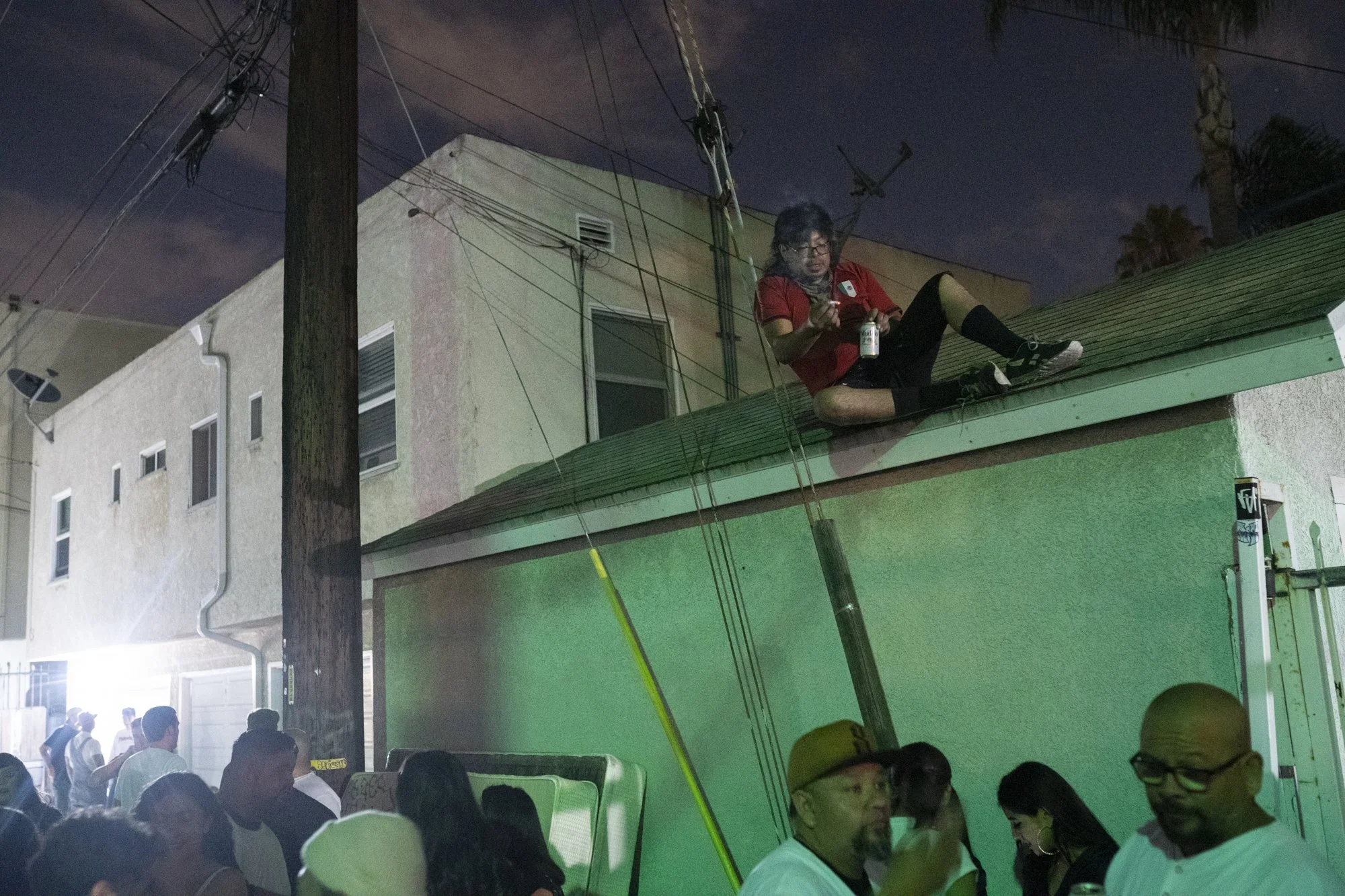 Person sitting on a rooftop overlooking a crowded Long Beach street at night during a barbershop event