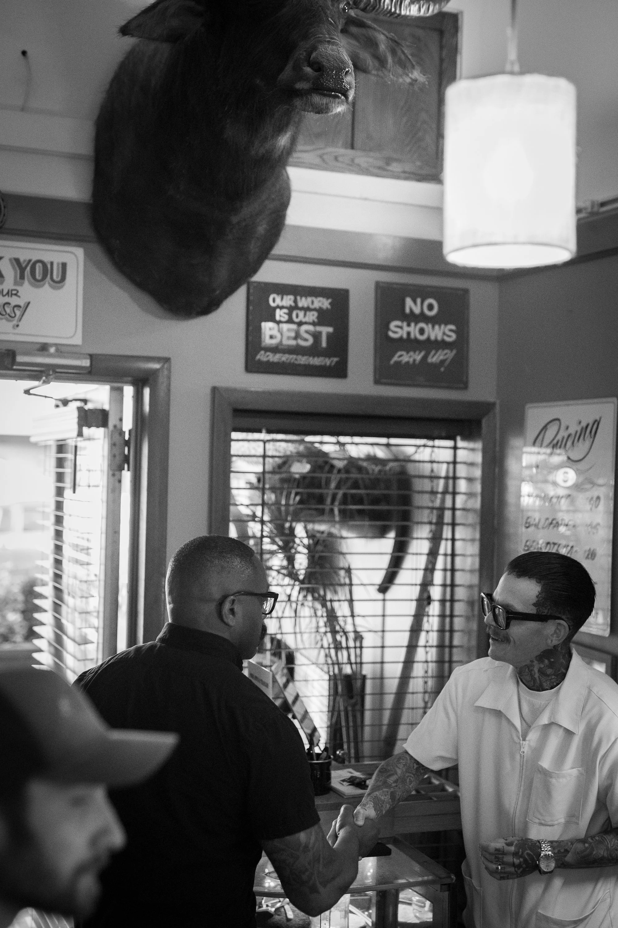 A barber in a white uniform shakes hands with a client inside Pugsly's barbershop.