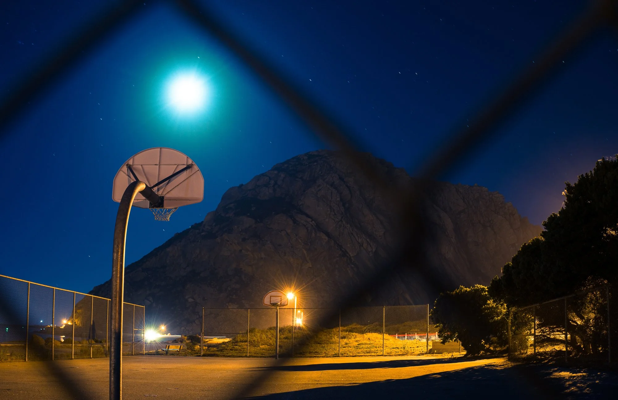 Basketball court with multiple hoops lit at night, with a large mountain rising behind it.