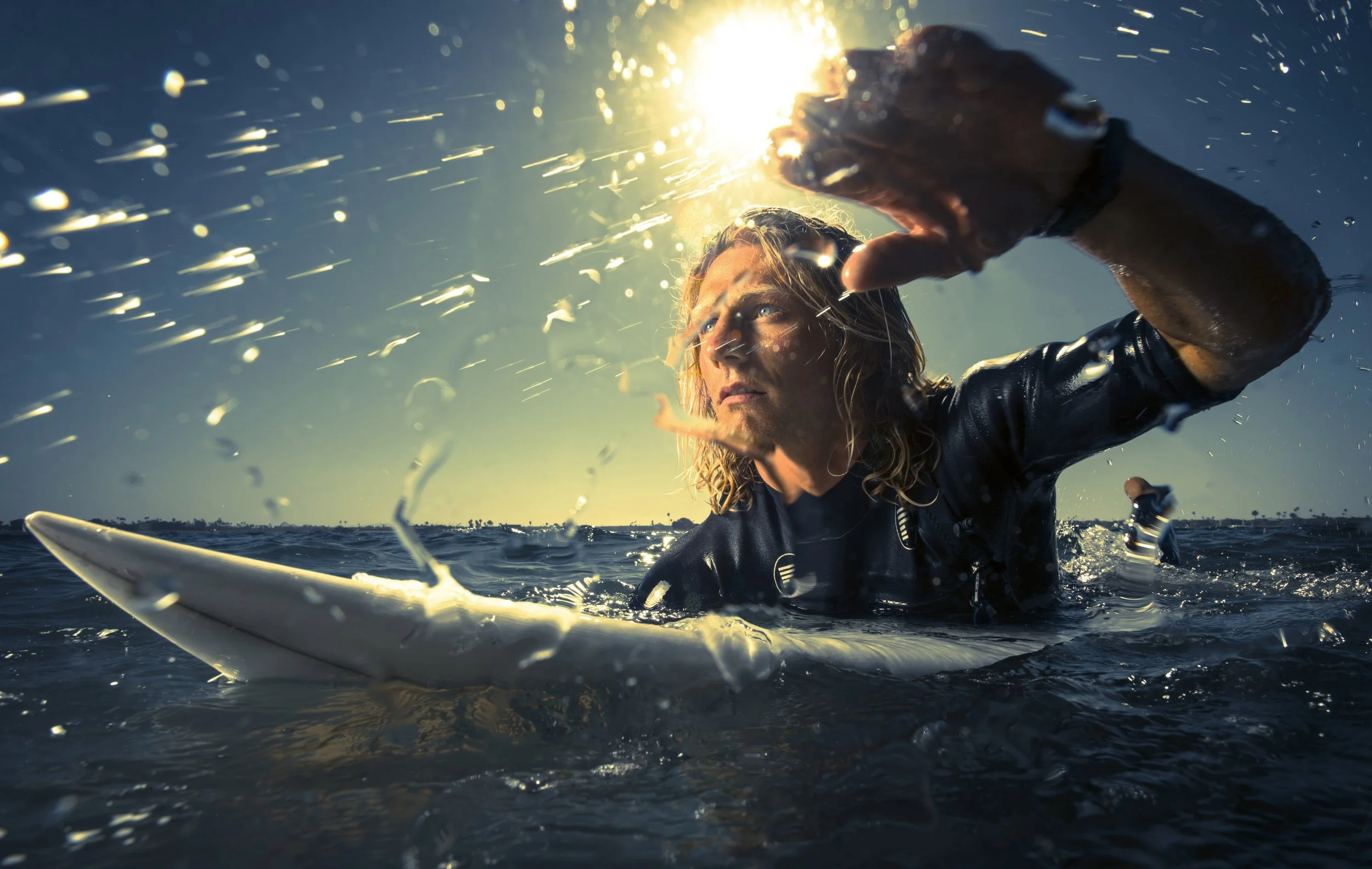 Surfer in ocean with water splashing and sun flare