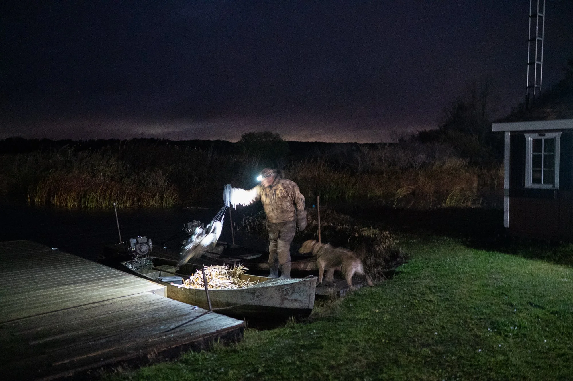 A duck hunter prepares boats before dawn beside marsh water during hunting season in Ontario