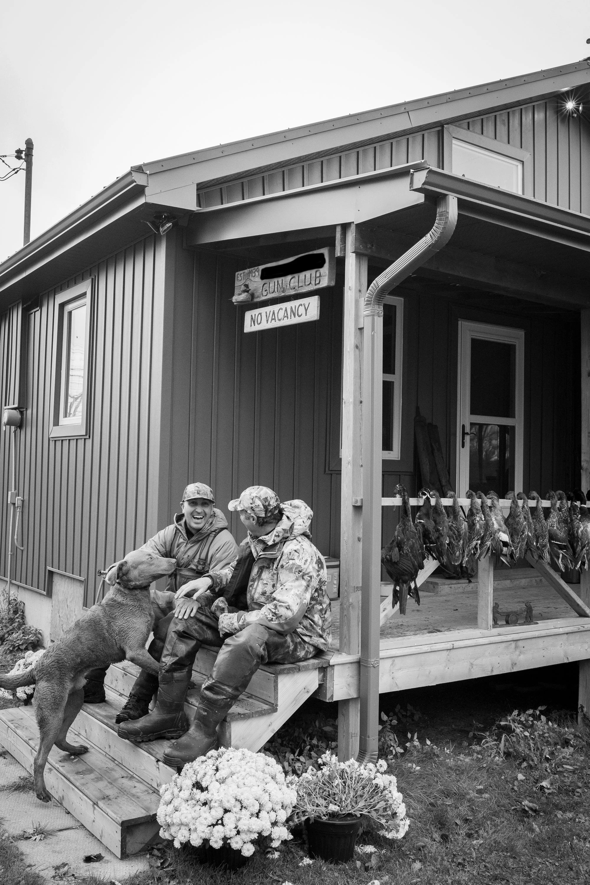 Hunters and a dog sitting laughing on the steps of the lodge after a day of hunting