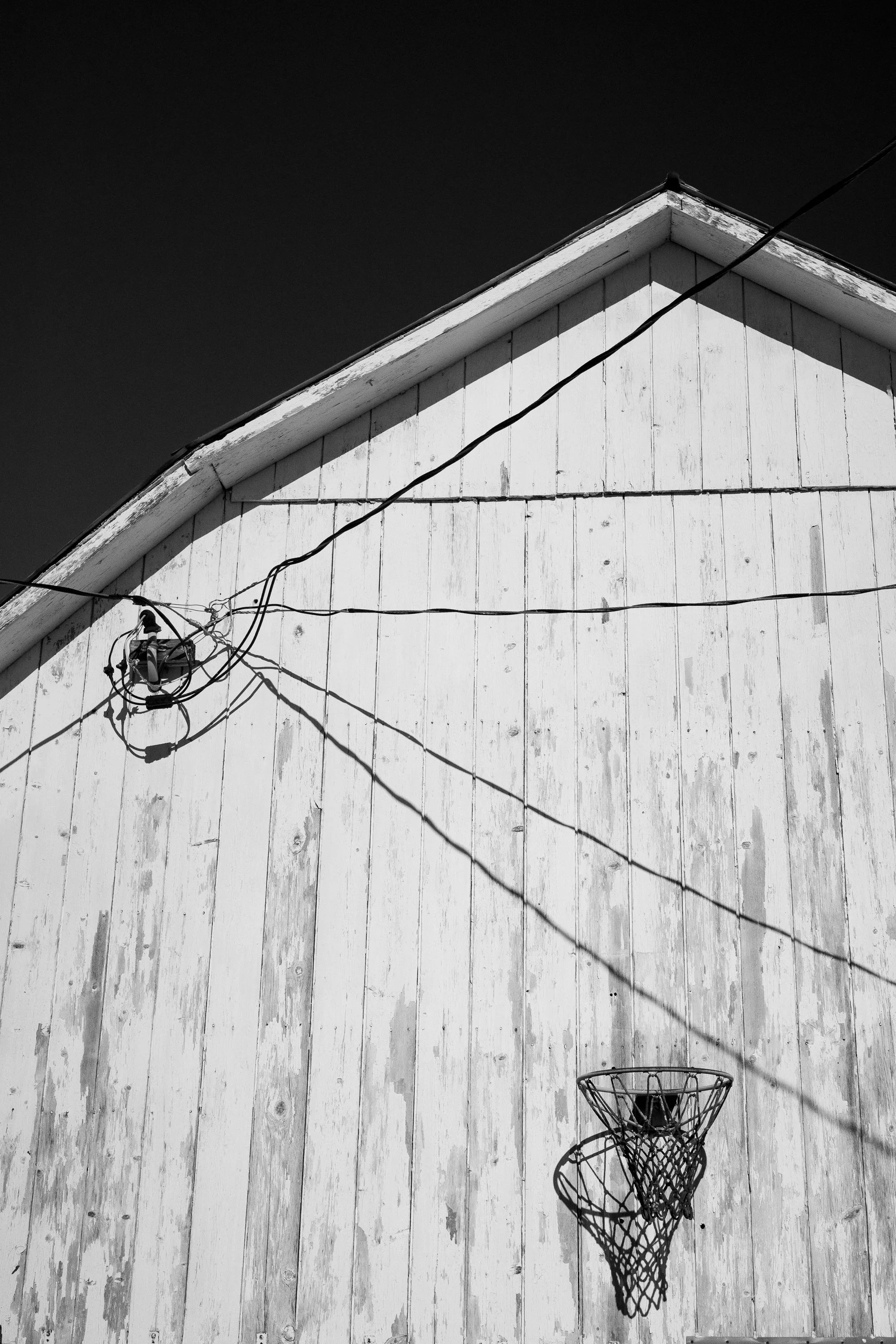 Basketball hoop mounted on a white barn wall beneath overhead wires