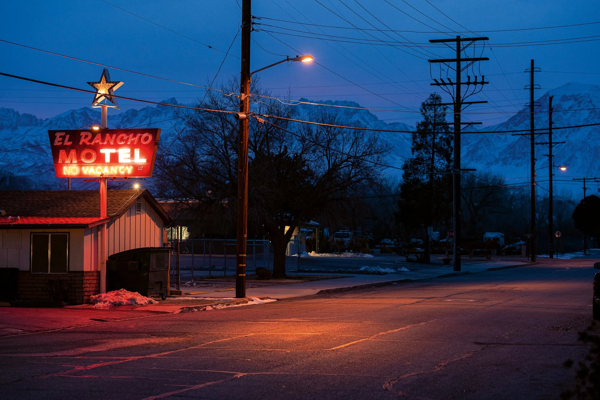 Neon motel sign glowing at night with mountains in background and empty street