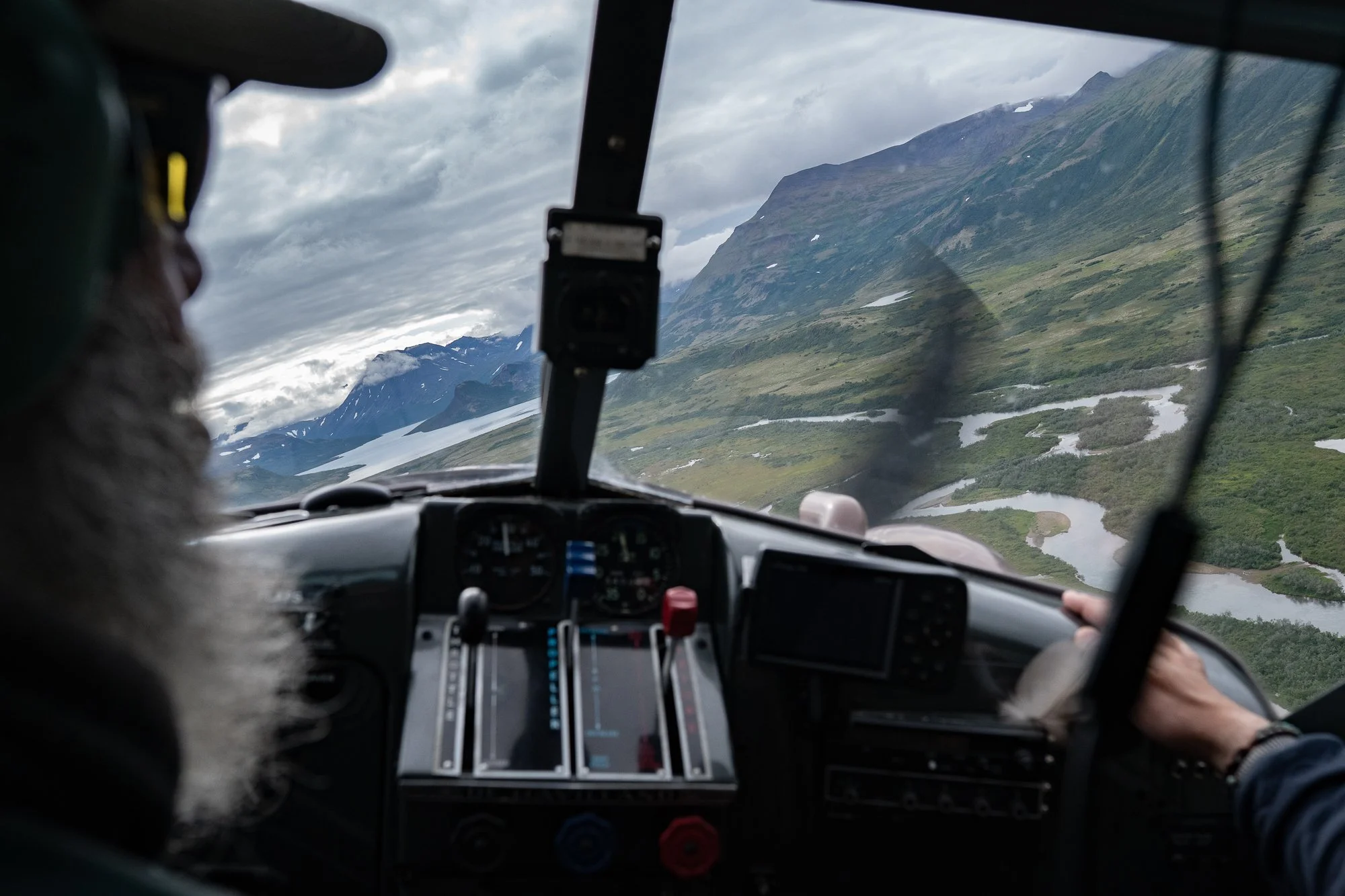 Pilot flying a small plane over mountains and rivers in Alaska
