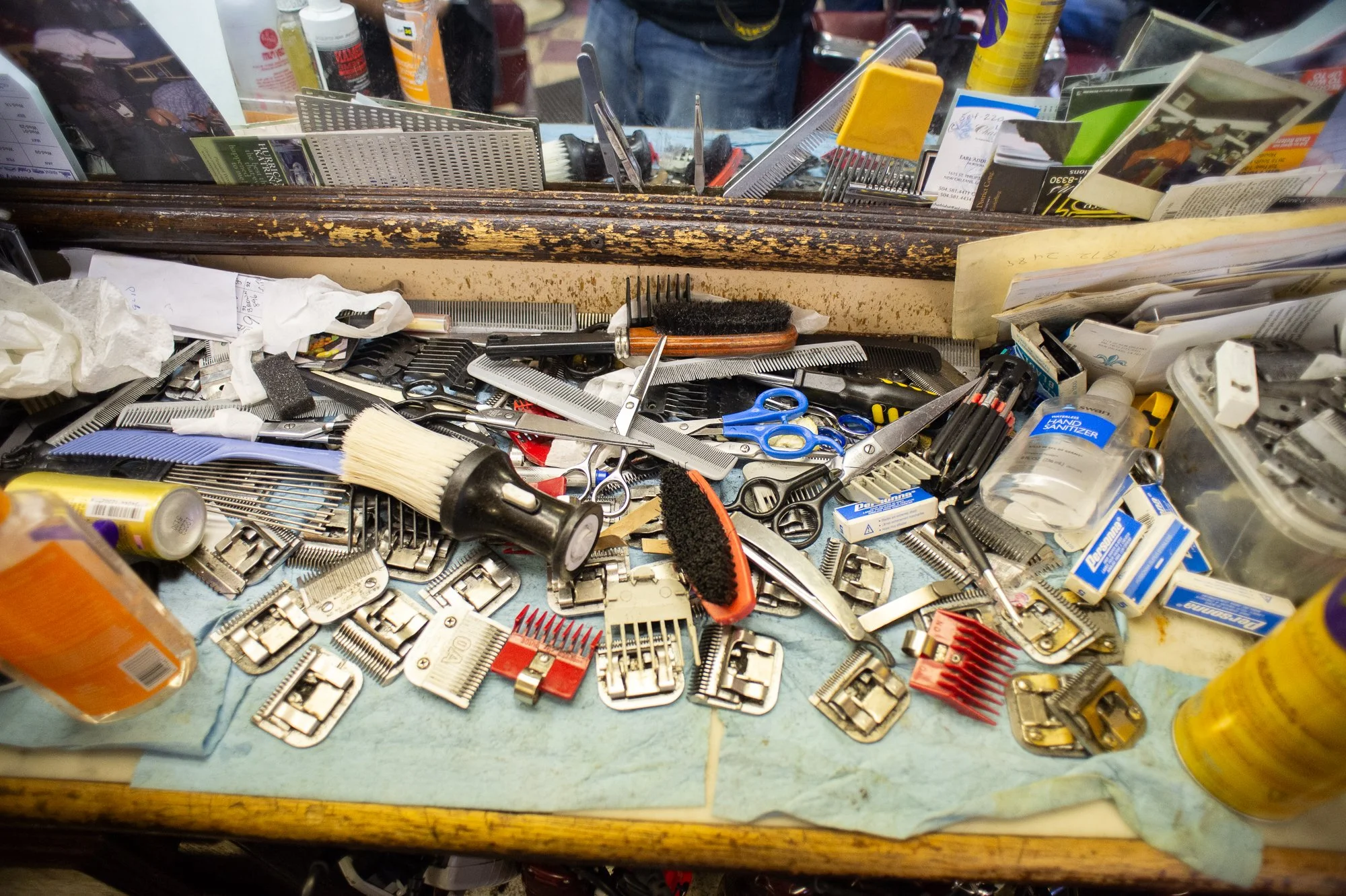 Close up of barber tools including clippers, combs, scissors, and brushes scattered across a worn counter