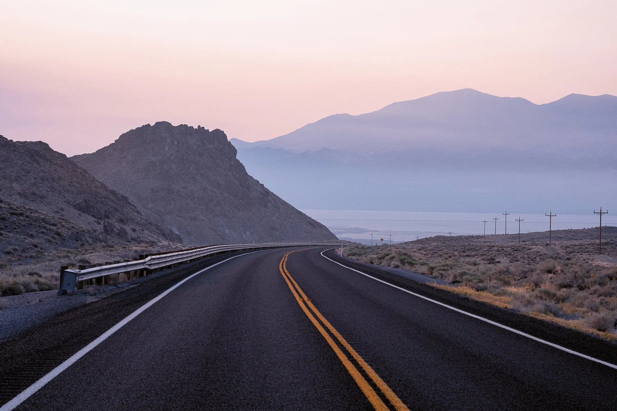 Winding mountain road overlooking desert basin at sunrise with soft light and distant peaks