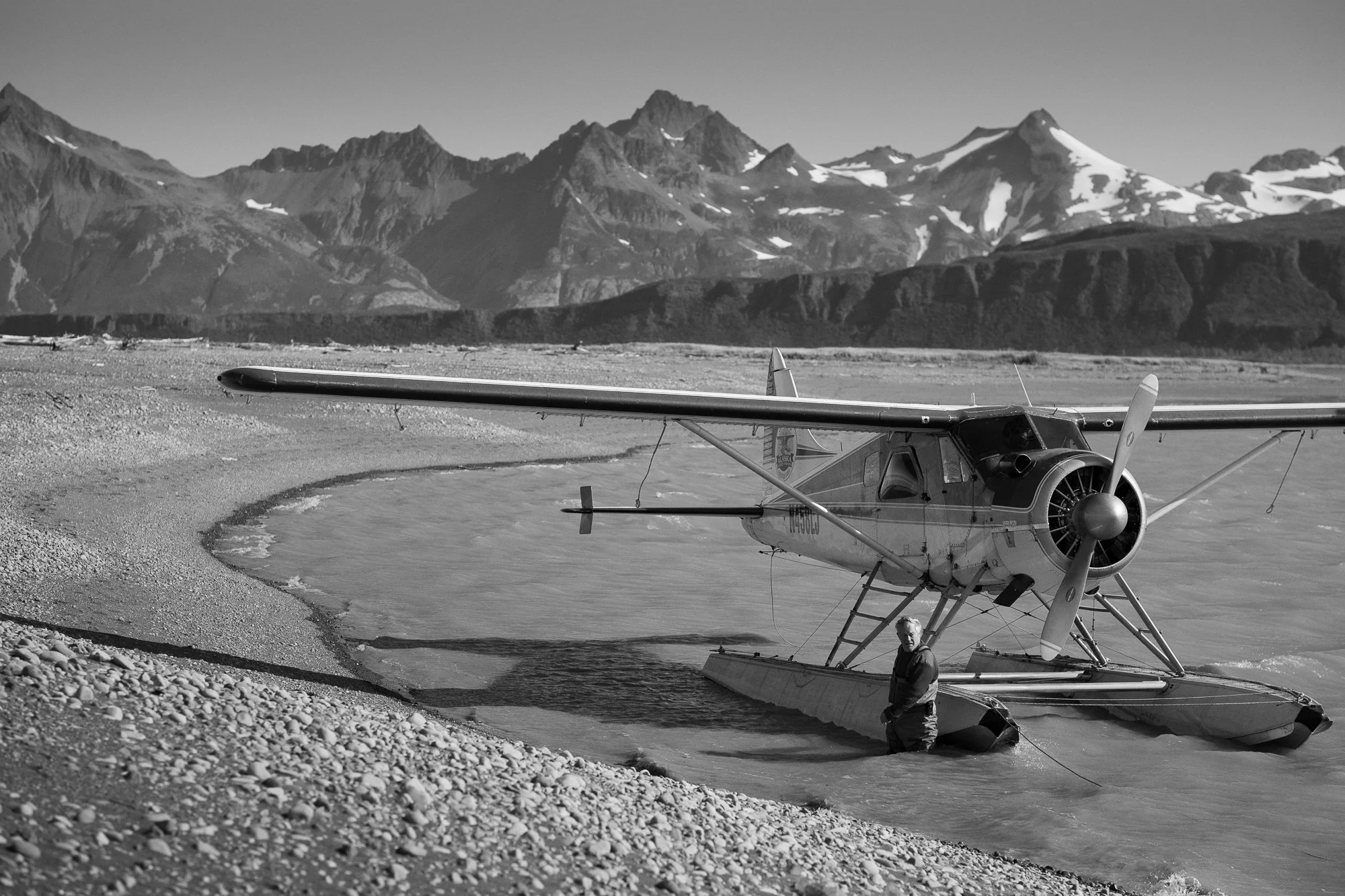 De Havilland Beaver float plane resting on a remote Alaskan river with mountains behind it