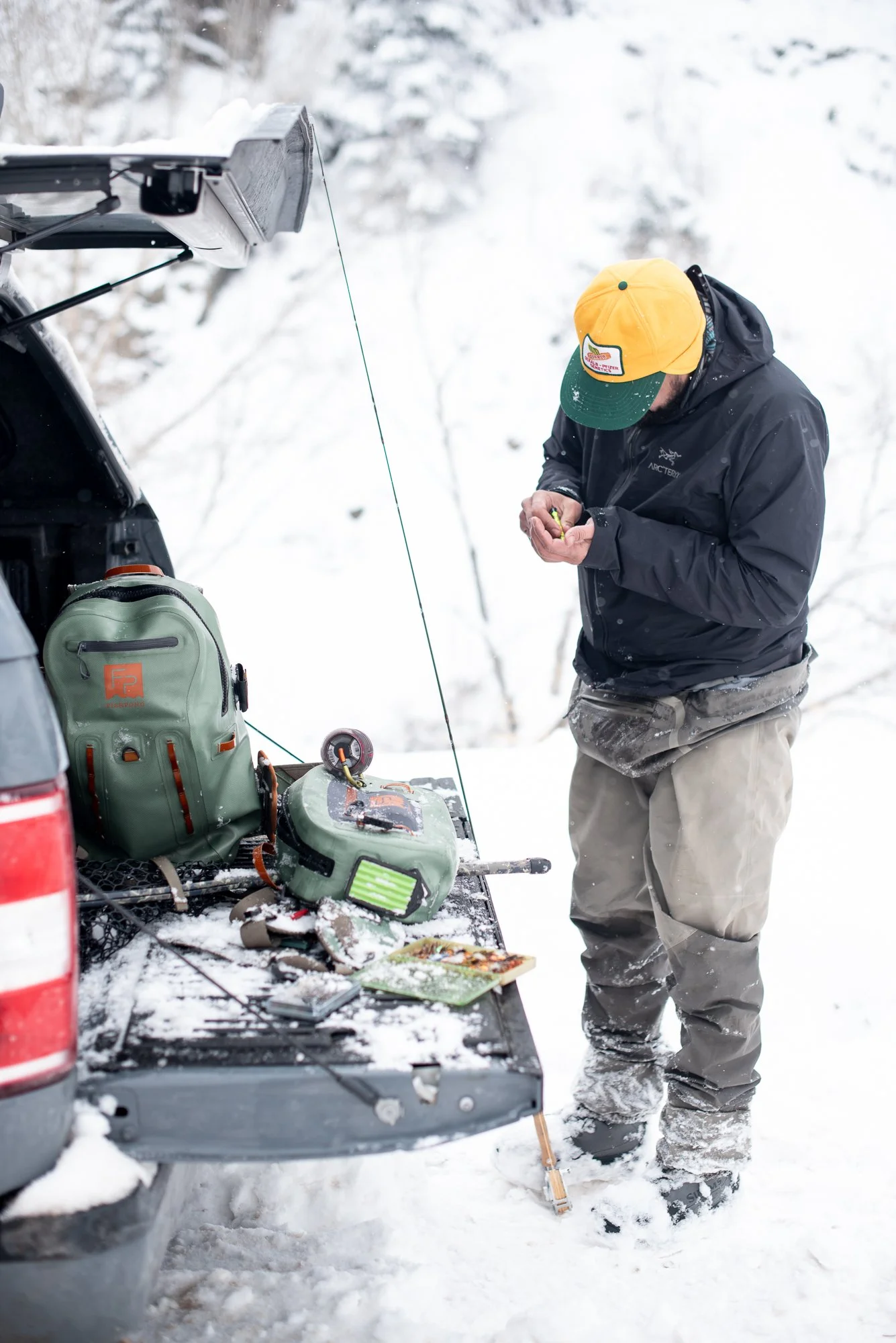 A fisherman prepares fly fishing gear at the back of a truck in snowy winter conditions near Clear Creek in Colorado.