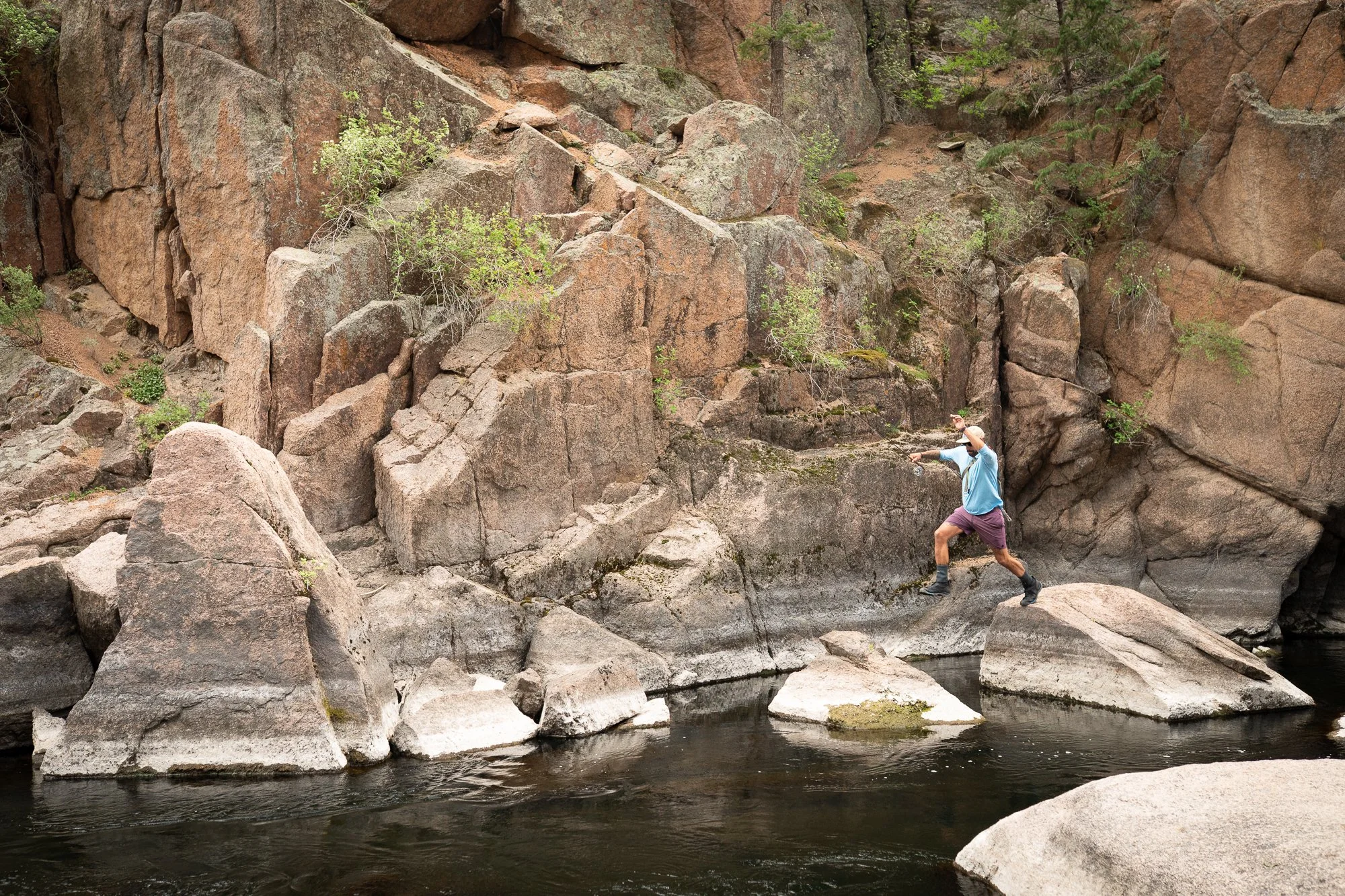 A fly angler casts from a rock ledge beside a river in a rocky canyon