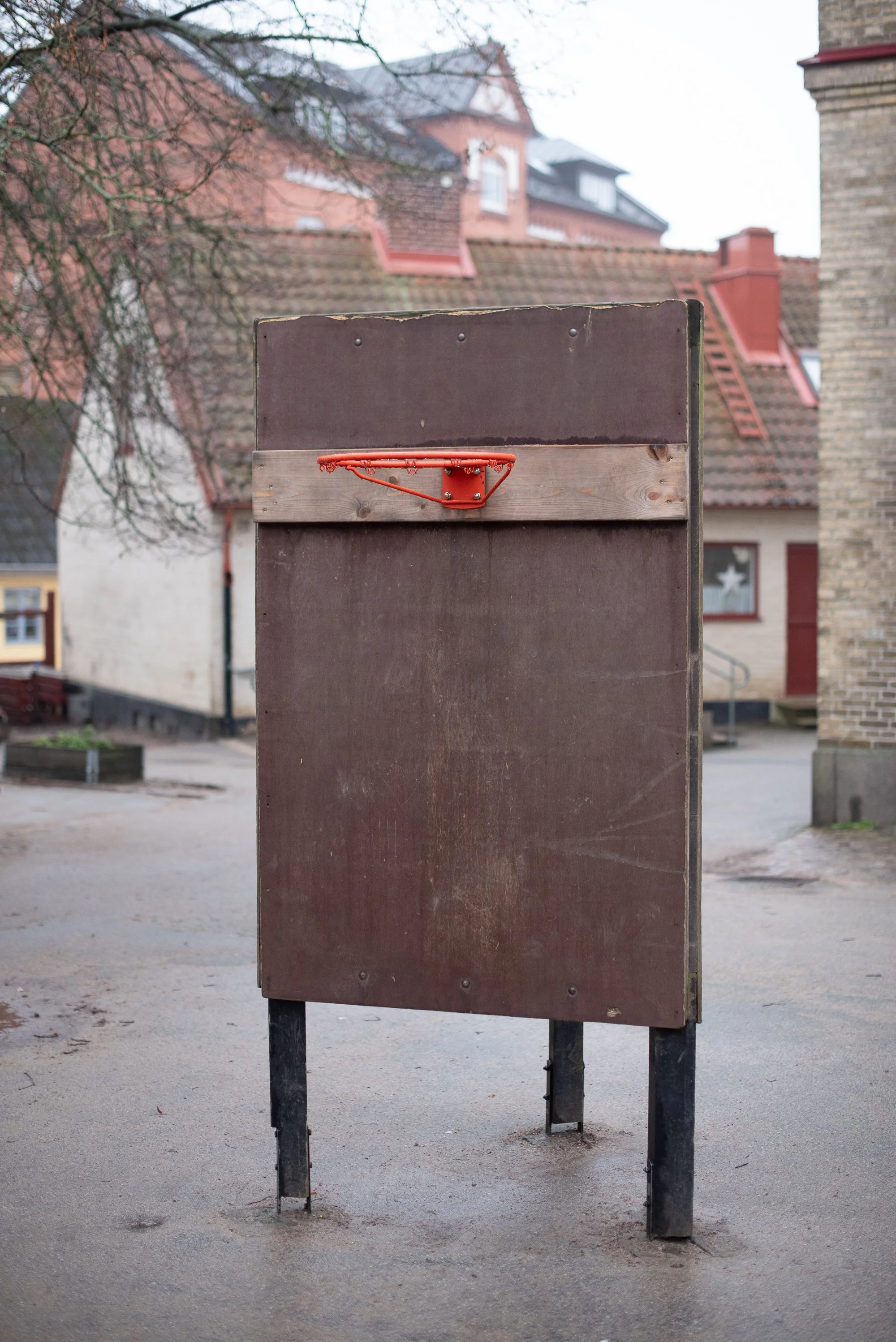 Handmade wooden basketball backboard with an orange rim photographed in a European residential setting.